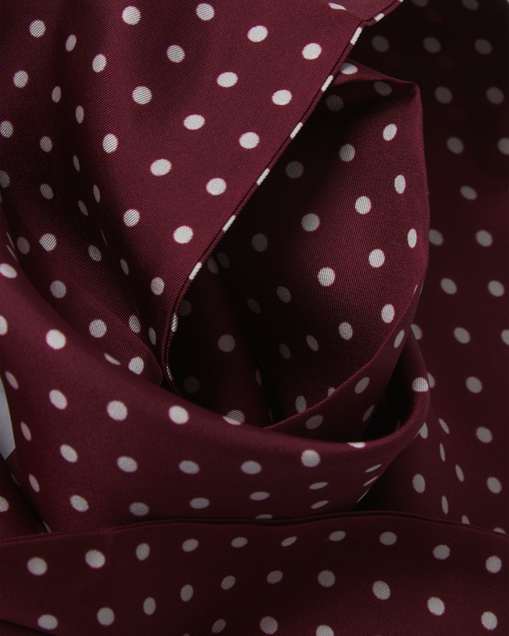 Ruffled close-up view of the Sapporo silk aviator scarf, presenting a closer view of the polka dot design in deep maroon with white dots and appealing lustre of the material.