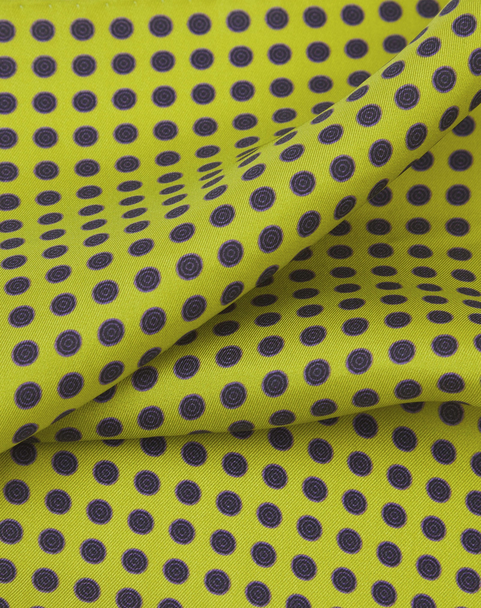 A ruffled close-up of the 'Skytree Lime' silk pocket square from SOHO Scarves, showing the 'bullseye target' charcoal and purple discs against a lime-green backdrop.