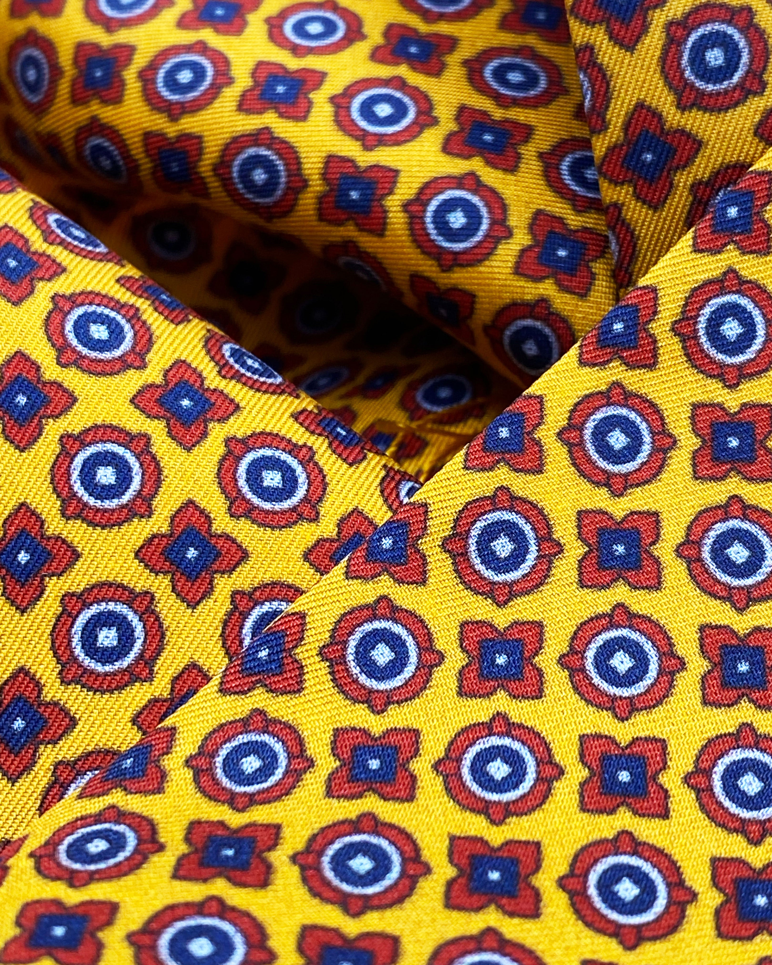 Ruffled close-up view of the Toshima silk pocket square, presenting a closer view of the small blue and red stylised floral patterns on a golden-orange ground.