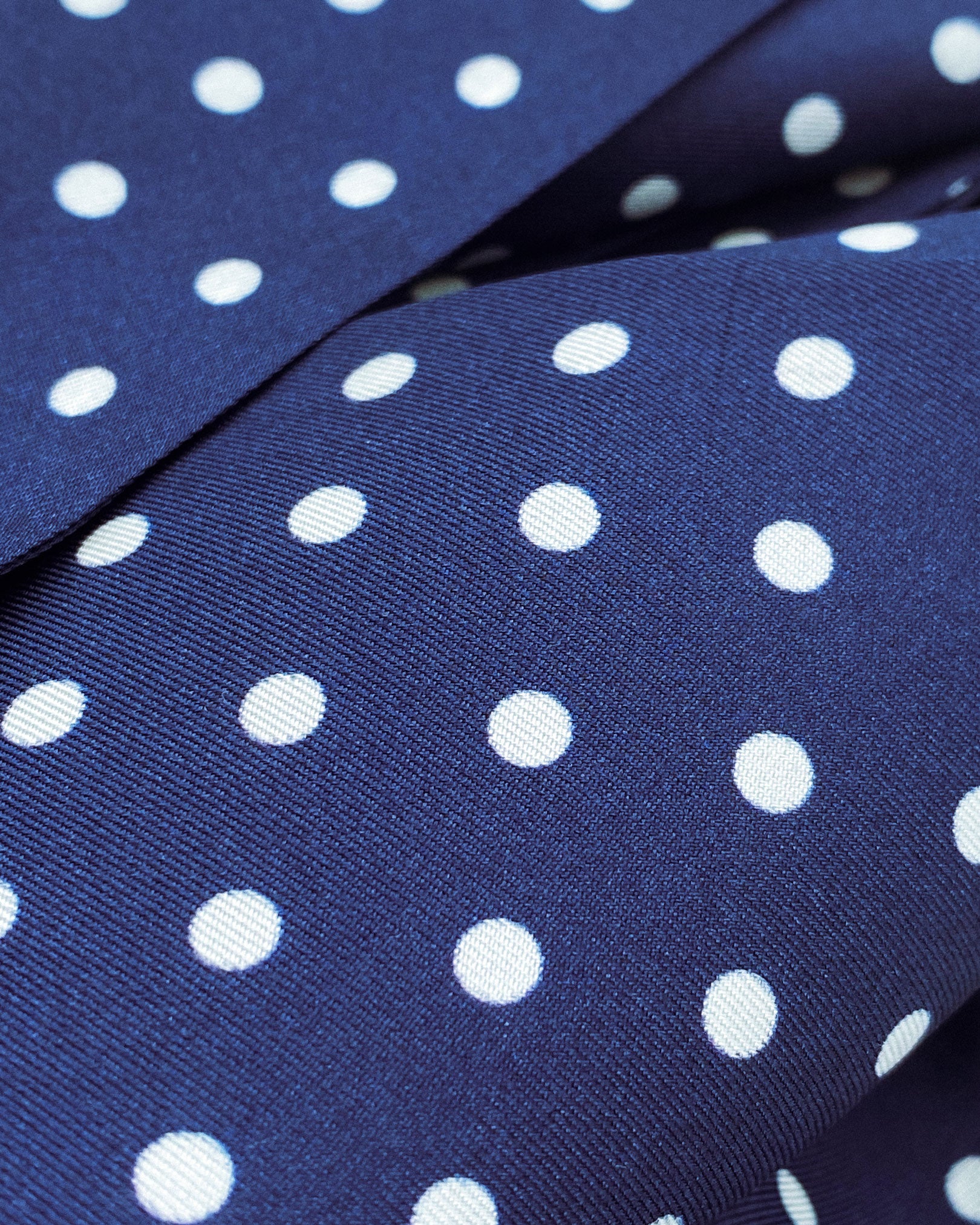 Ruffled close-up view of the 'Westminster' silk aviator scarf, presenting a closer view of the polka dot design in navy-blue with white spots and subtle lustre of the material.