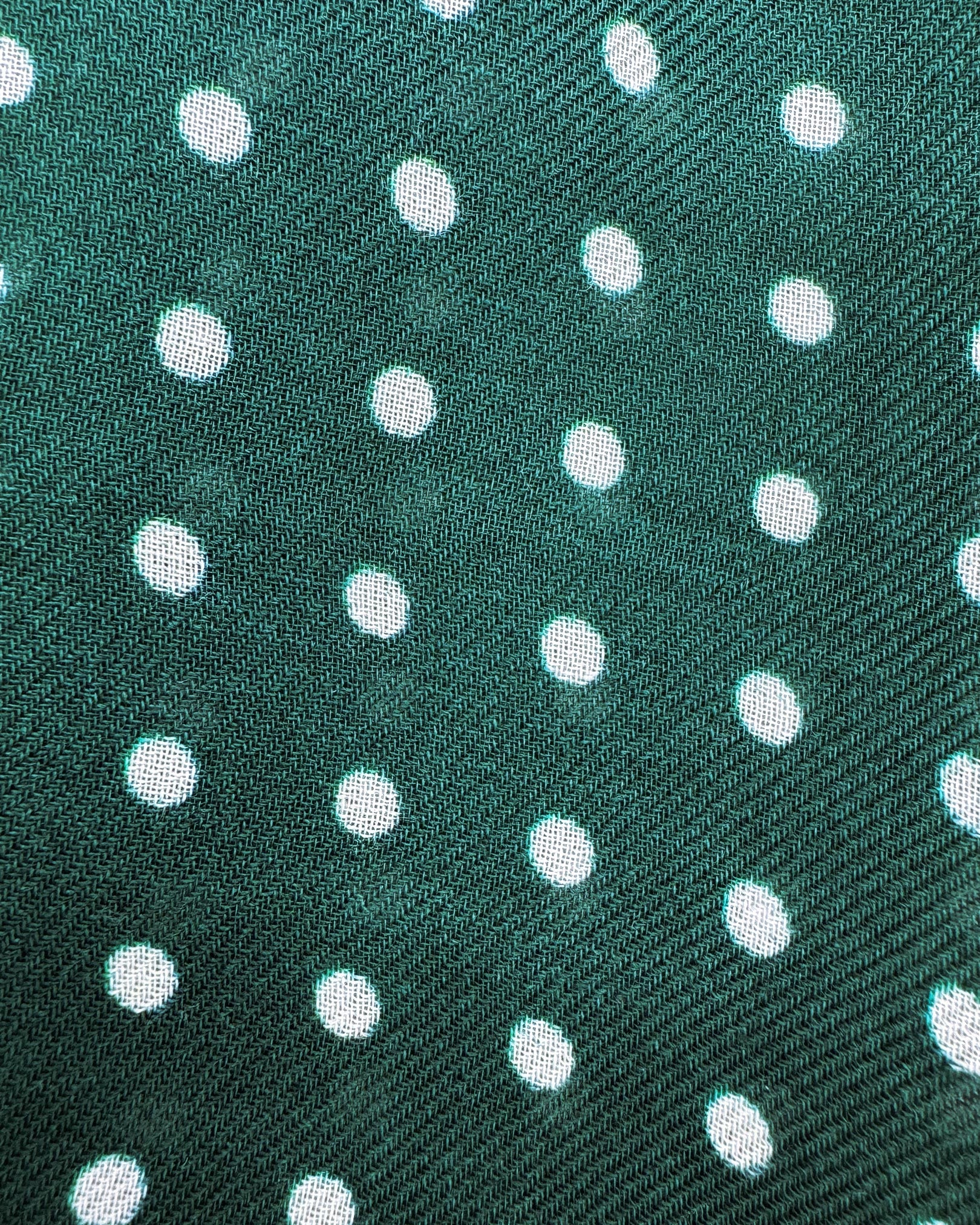 A flat, close up view of 'The Westminster RG' wide scarf. Clearly showing the modal and wool fabric and attractive white polka dot pattern against a racing green background.