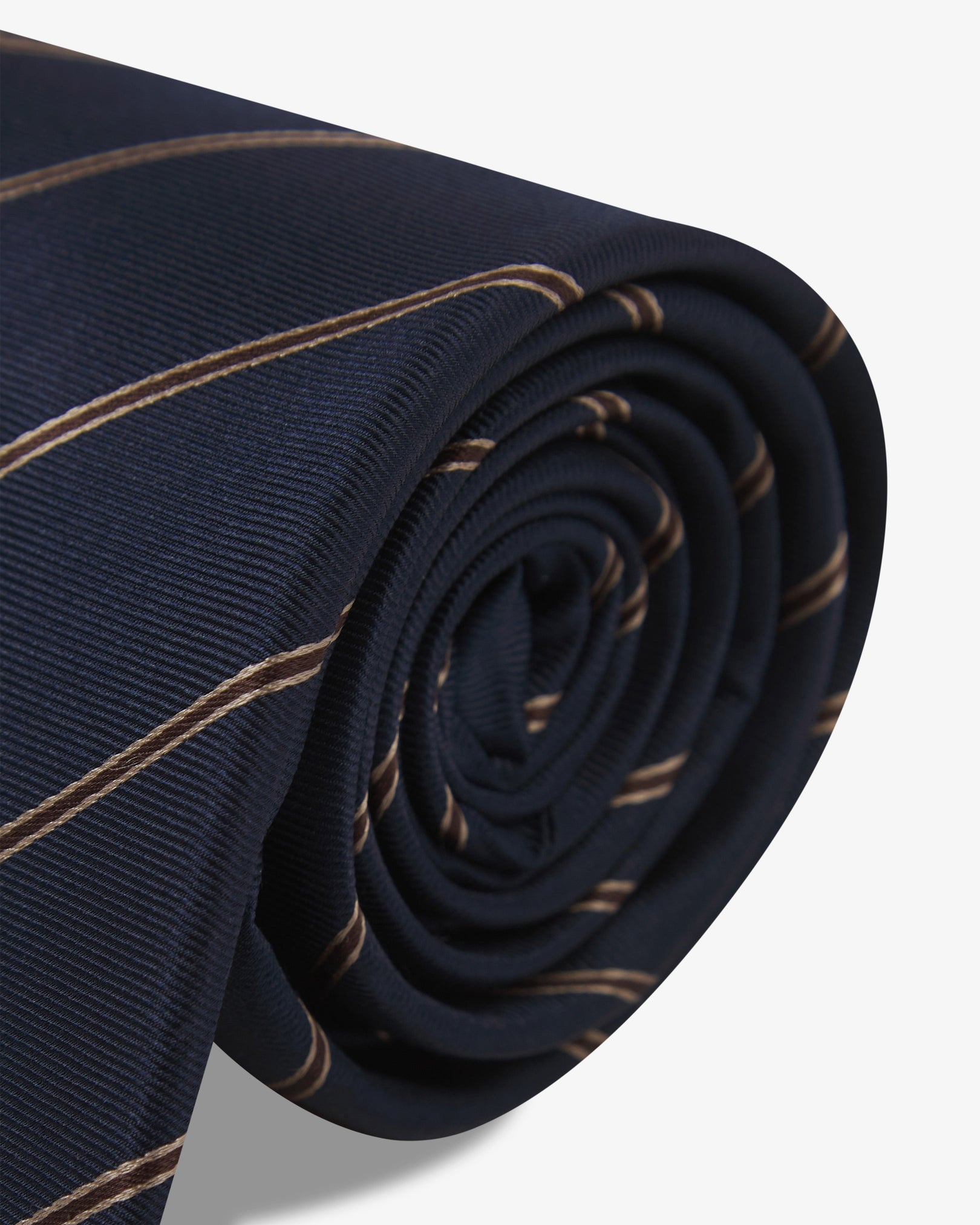 The 'Coltraine Mahogany Haze' silk neck tie neatly coiled with a clear view of the silk weave and gold and brown stripes against a black background.