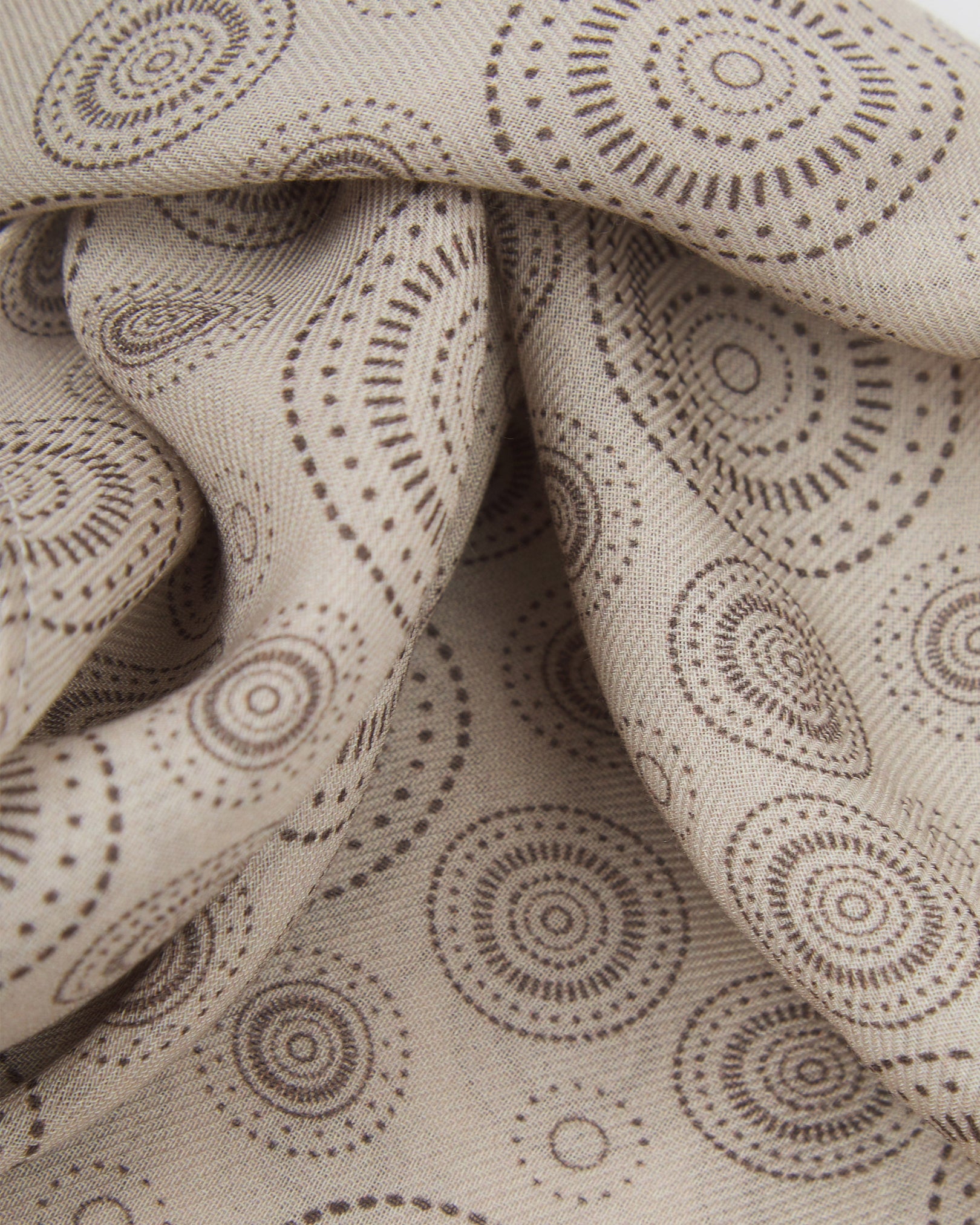 A ruffled close-up of the 'Circles' cream bohemian wide scarf, showing the soft modal and wool blend fabric with concentric Op art-inspired disc motifs in dark grey on a pale cream background.