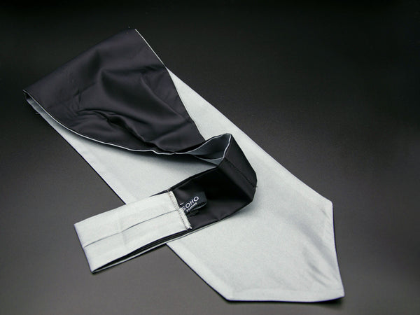 Pale grey 'Bilbao' single pointed Ascot tie arranged diagonally with wide point in foreground. Narrow end of tie folded back and over to reveal dark lining and 'SOHO Scarves' branding label.