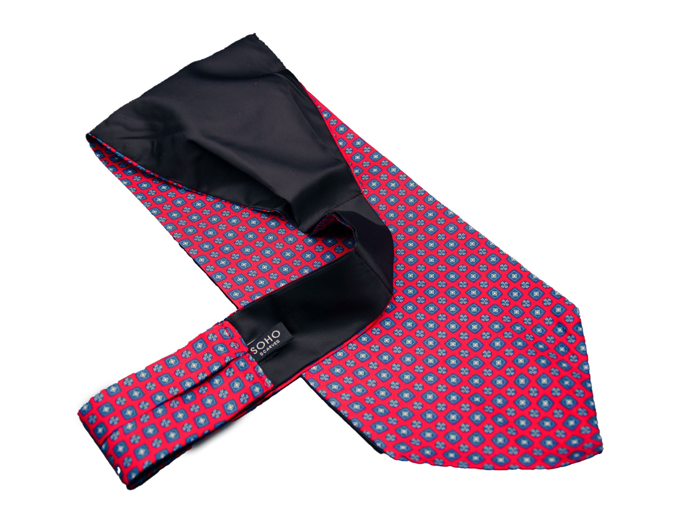 Bright red 'Canaria' single pointed Ascot tie arranged diagonally with wide point in foreground with clear view of blue motifs made up of tiny squares, disks and diamonds.