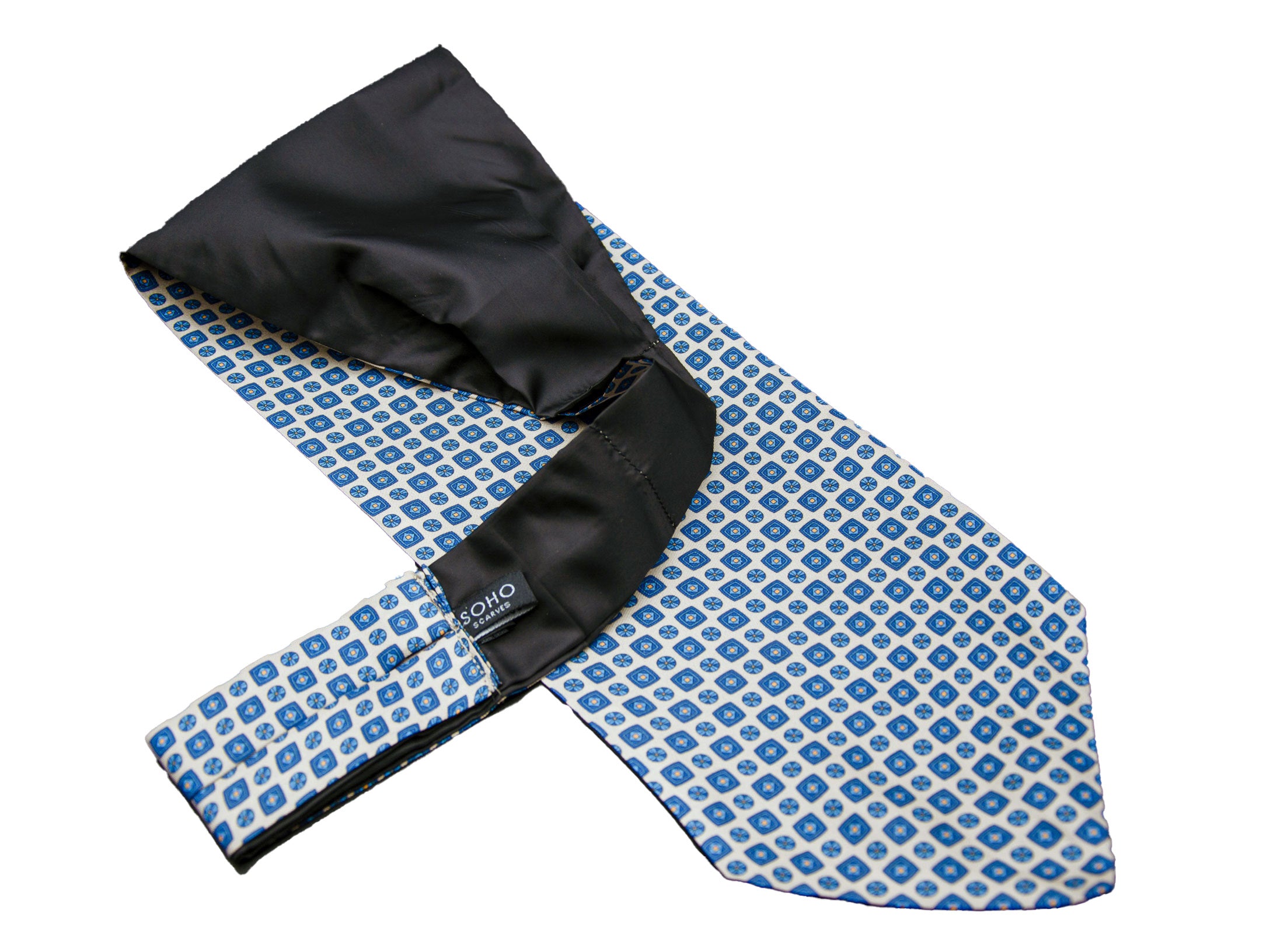 Off-white 'Malaga' single pointed Ascot tie arranged diagonally with wide point in foreground with clear view of blue motifs made up of tiny squares, disks and diamonds.