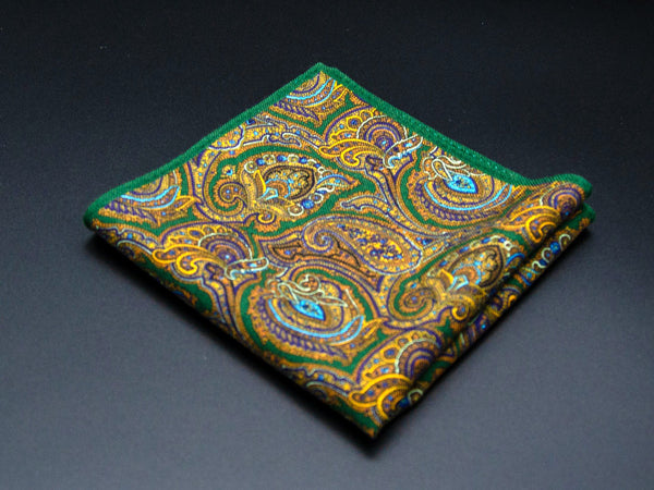 Perspective flat view of 'The Kingly' wool pocket square arranged in a diamond shape, clearly showing the paisley and gold, green and brown pattern and narrow green border.