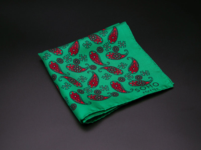 Pure silk 'Fes' pocket square folded showing simple red paisley 'tears' interdispersed with decorative floral patterns on a vibrant green ground. SOHO Scarves branding clearly visible on bottom-right.