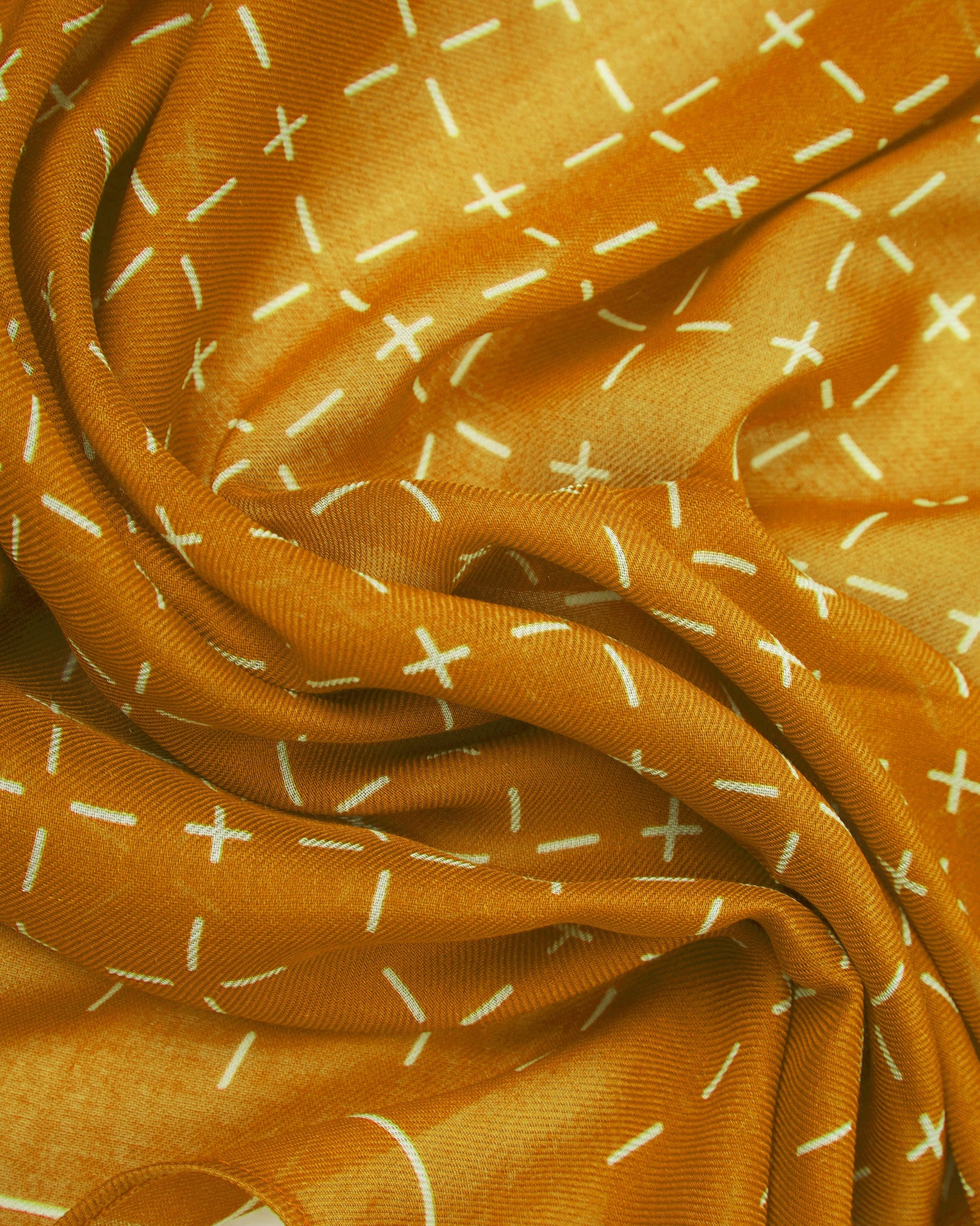 A ruffled close-up of the 'Crosses in Dust' modal and wool bandana from SOHO Scarves, highlighting the soft modal and wool blend fabric with a repeating geometric grid pattern of dashes and crosses in warm dust tones.