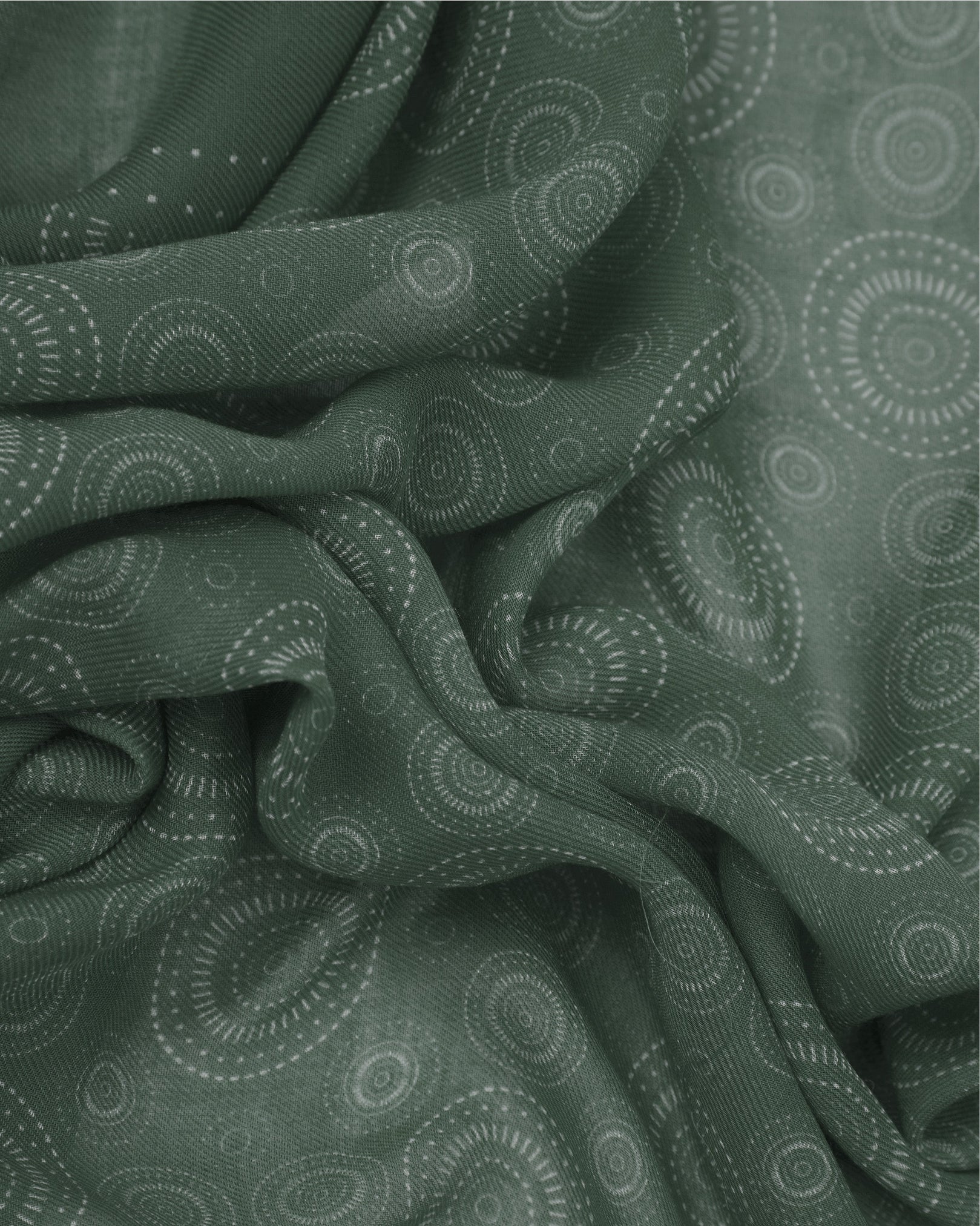 A ruffled close-up of the 'Circles' evergreen bohemian wide scarf, showing the soft modal and wool blend fabric with concentric Op art-inspired disc motifs in layered evergreen tones.