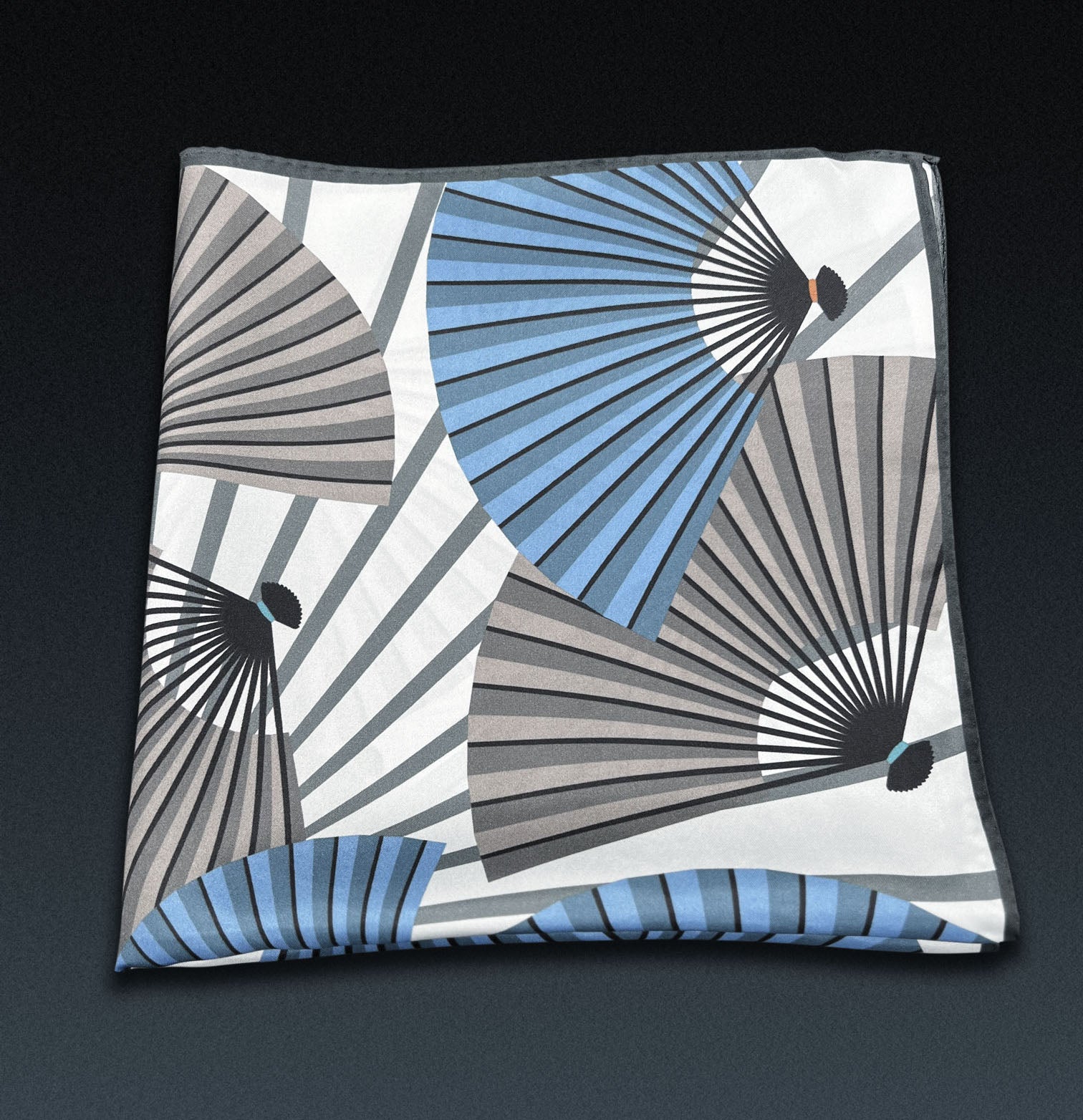 'The Fan' neckerchief folded into a quarter, showing layered blue and grey fan motif on an off-white background.