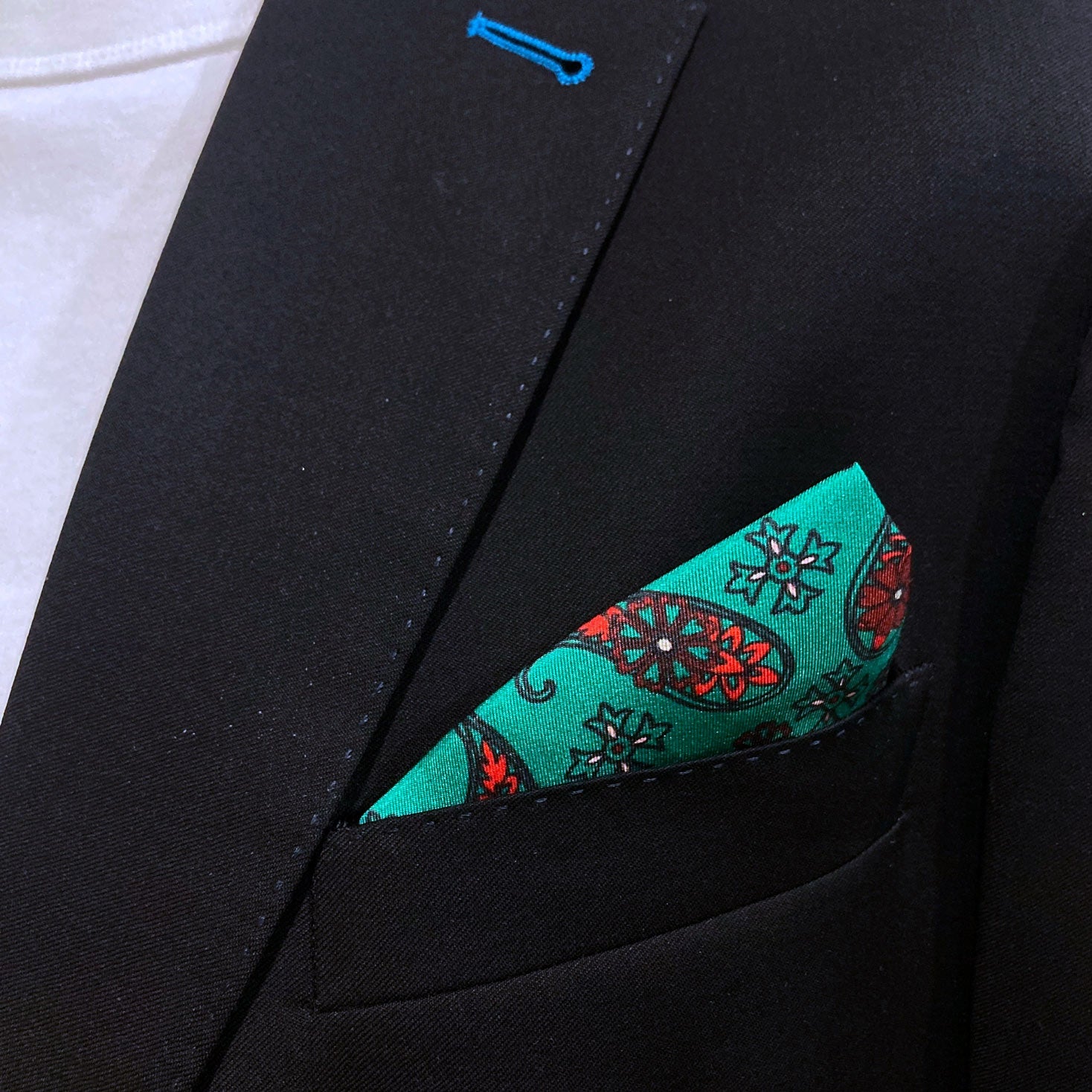 Close-up of 'Fes' silk pocket square in breast pocket of dark suit jacket.