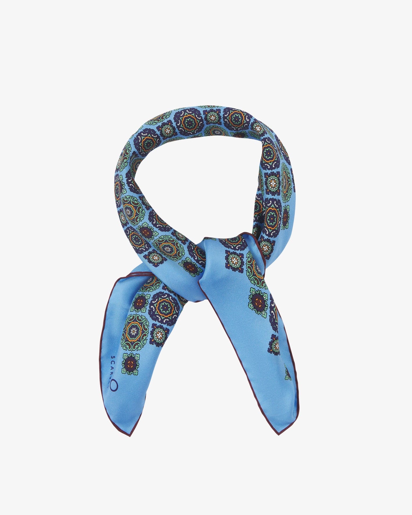 The 'Fitzrovia' neckerchief looped and knotted, revealing the bold medallion motifs in navy, forest green, and ochre against a cool Leyland blue silk.