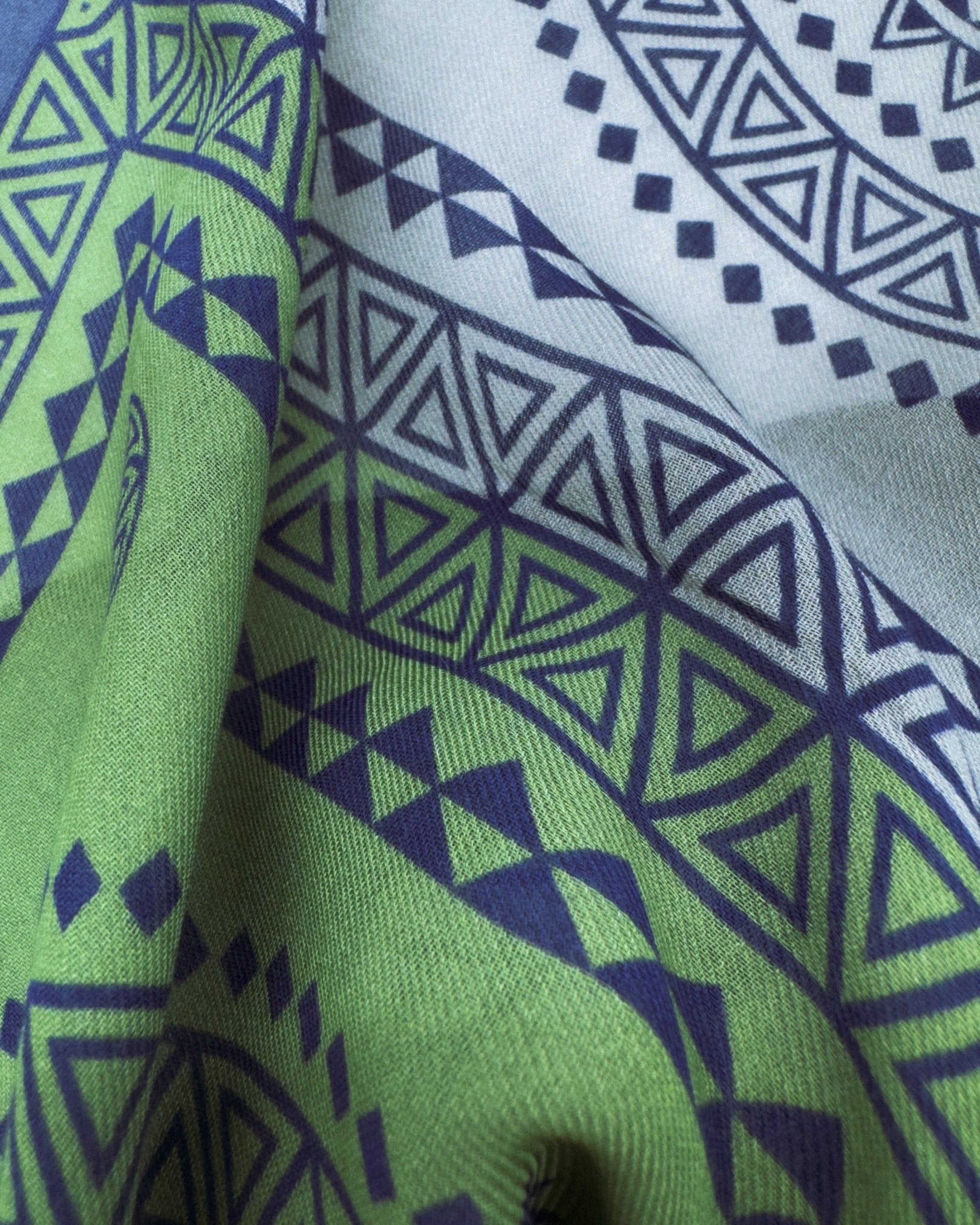 A flat view of 'The Lublin' bandana. Clearly showing the Aztec geometric triangular and diamond patterns in blue, green, and violet with a clear view of the modal-wool weave.