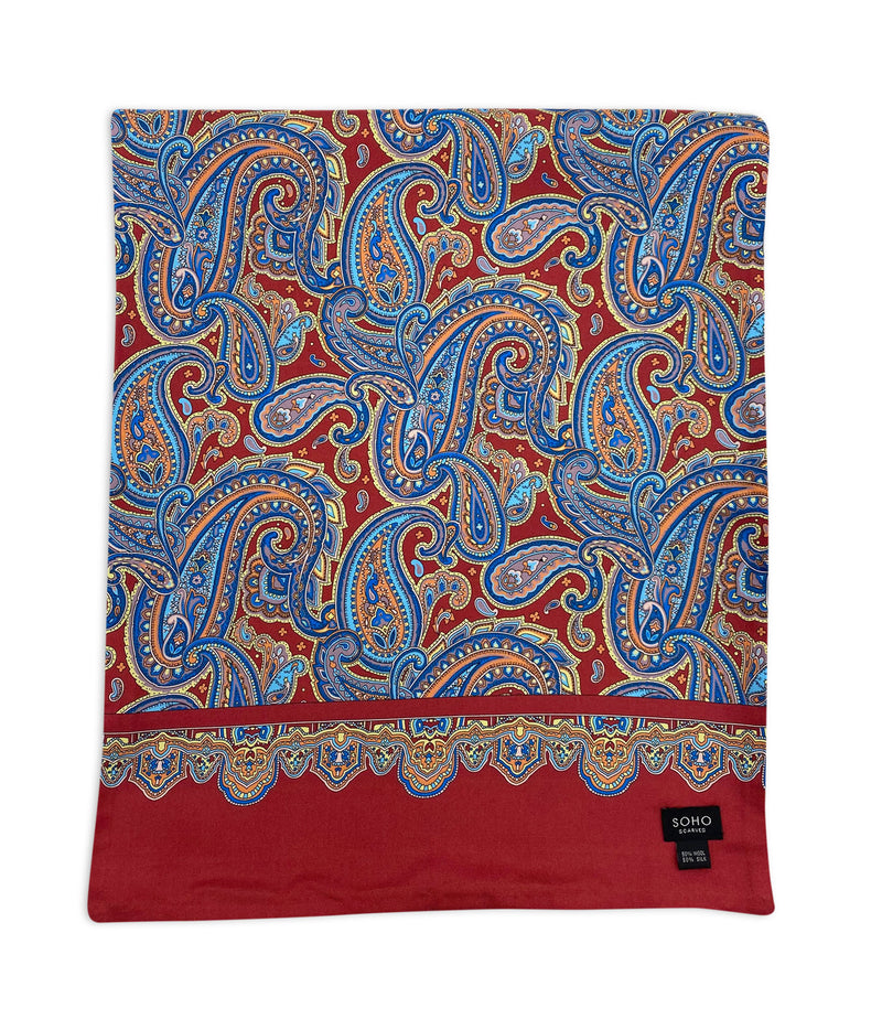 'The Hedge' wide dress scarf arranged in a square shape with a focus on the intricate multicoloured patterns and ornate border set on a deep red ground with logo in bottom right corner.
