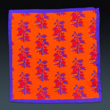 Fully unfolded 'Severn' silk pocket square, showing the repeat motif in purple and red on a striking reddish-orange background.