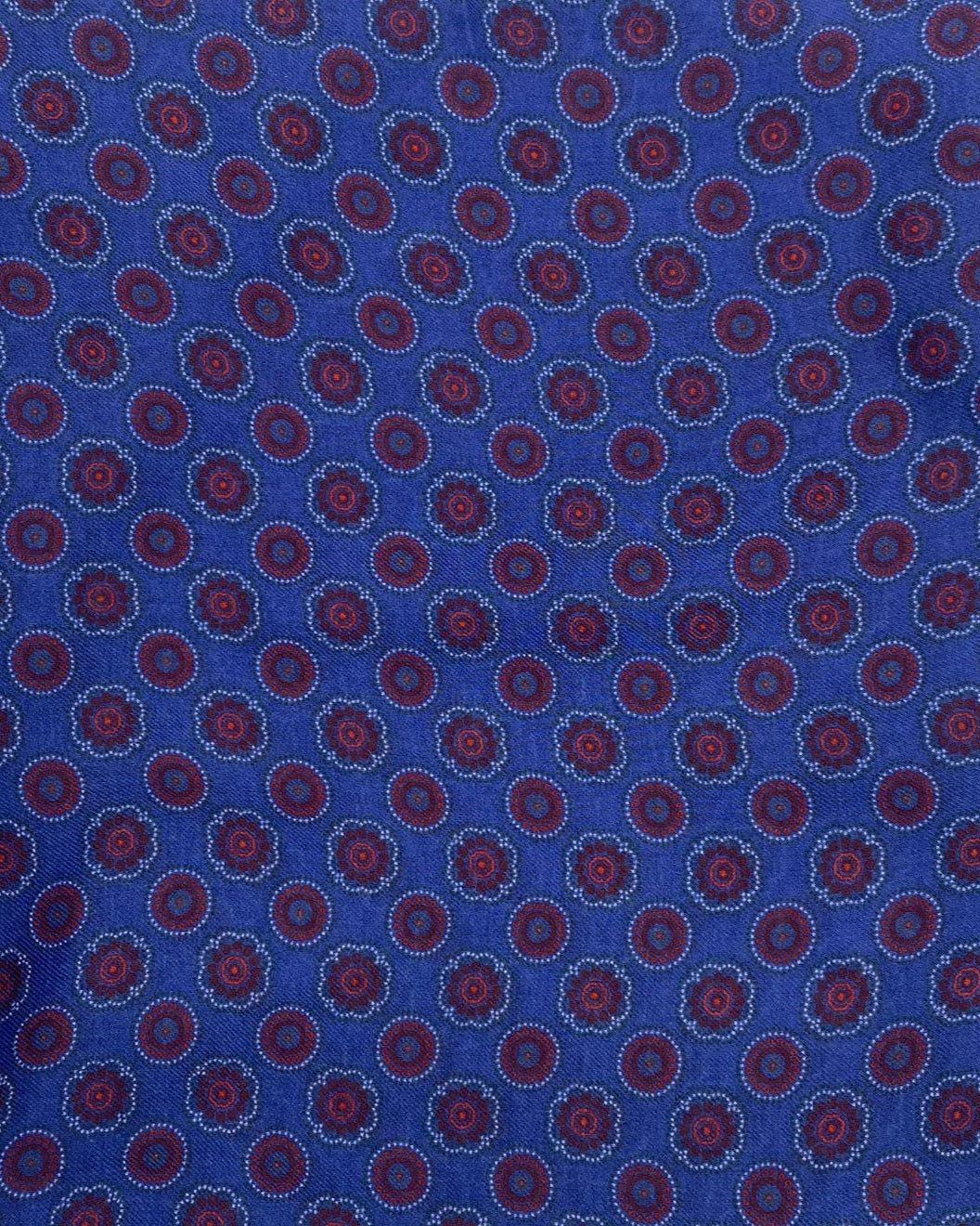 A flat, folded view of 'The Bellevue' boho wide scarf on a blue background. Clearly showing the circular red patterns and floral inspired patterns.