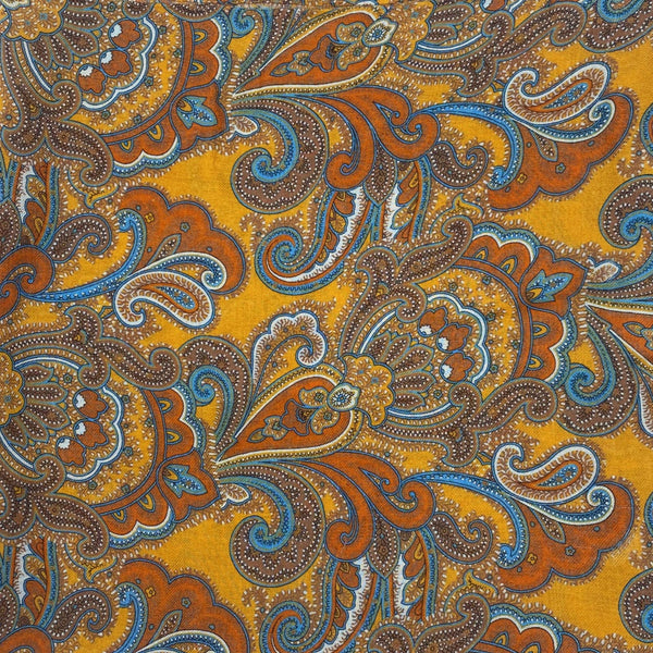 A flat, folded view of 'The Carnaby' boho wide scarf. Clearly showing the large swirls of paisley patterns on a gold-yellow background.