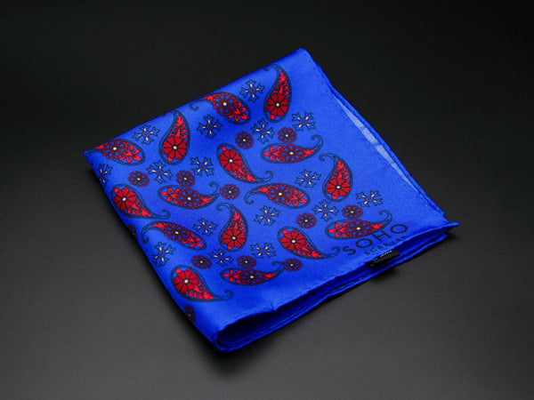 Pure silk 'Marrakesh' pocket square folded showing simple red paisley 'tears' interdispersed with decorative floral patterns on a bright blue ground. SOHO Scarves branding clearly visible on bottom-right.