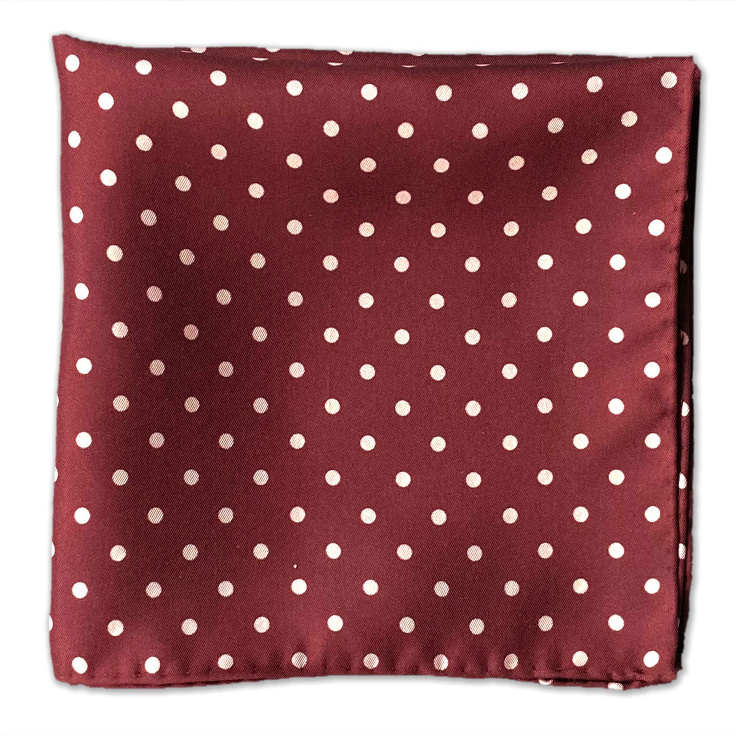 Flat view of the 'Sapporo' polka dot patterned silk pocket square set on a deep red fabric background.