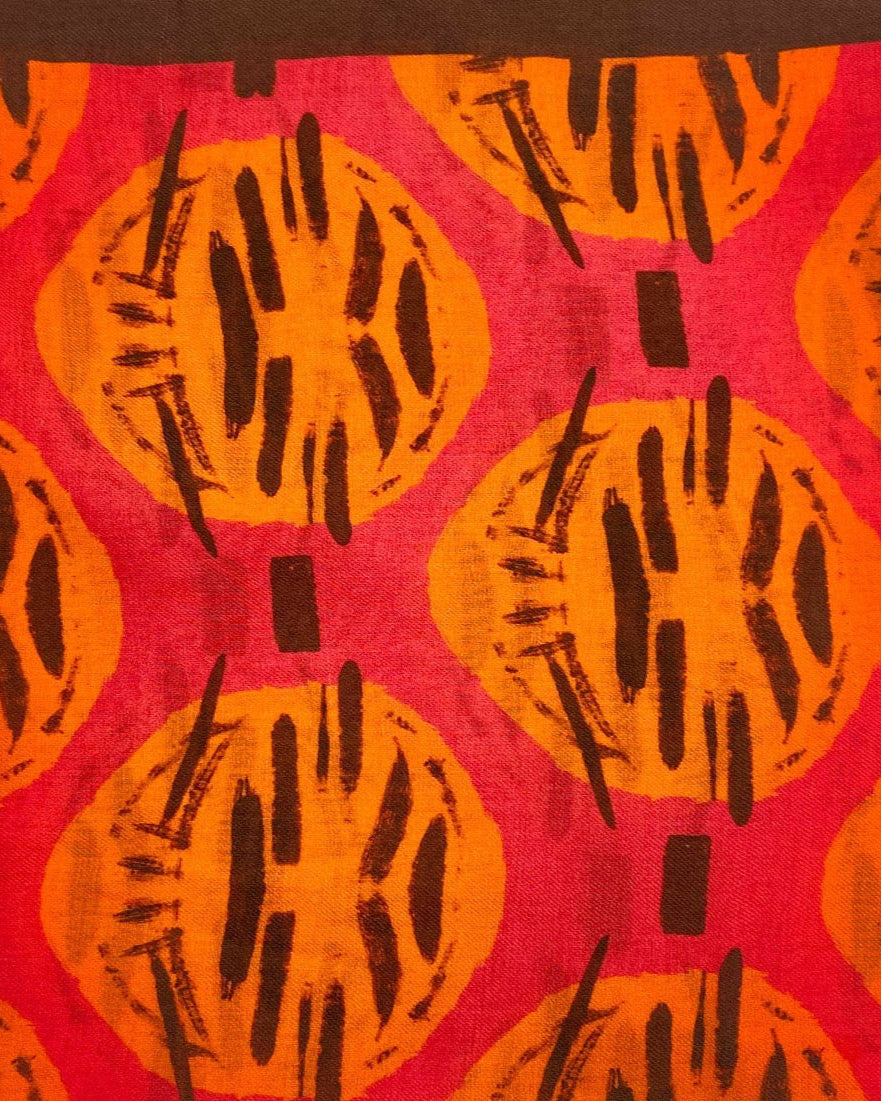 A flat, folded view of 'The Sierra' bandana. Clearly showing the primitive Aztec inspired pattern in red, orange and brown.