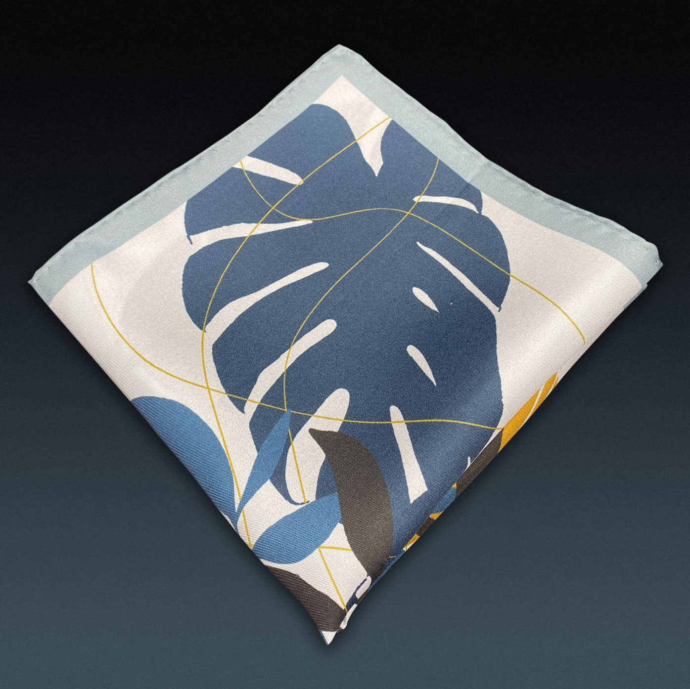 Folded 'Tyne' silk pocket square from SOHO Scarves, showing the floral-sun pattern. Placed on a dark background.