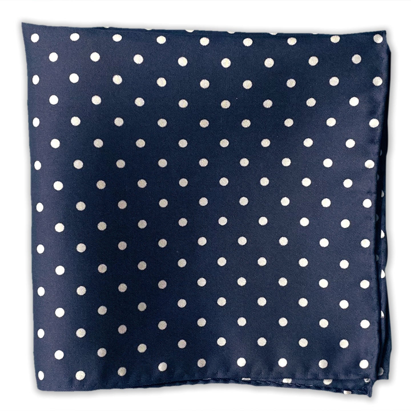 Flat view of the 'Westminster' polka dot patterned silk pocket square set on a deep blue fabric background.