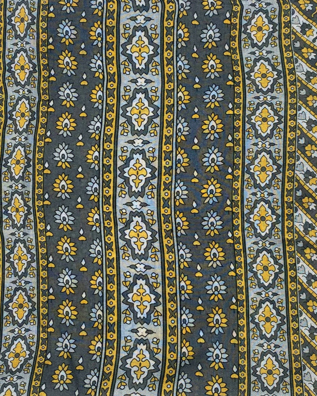 A flat, folded view of 'The Whitehorse' boho wide scarf. Clearly showing the decorative and floral-inspired patterns in yellow, grey and silver.