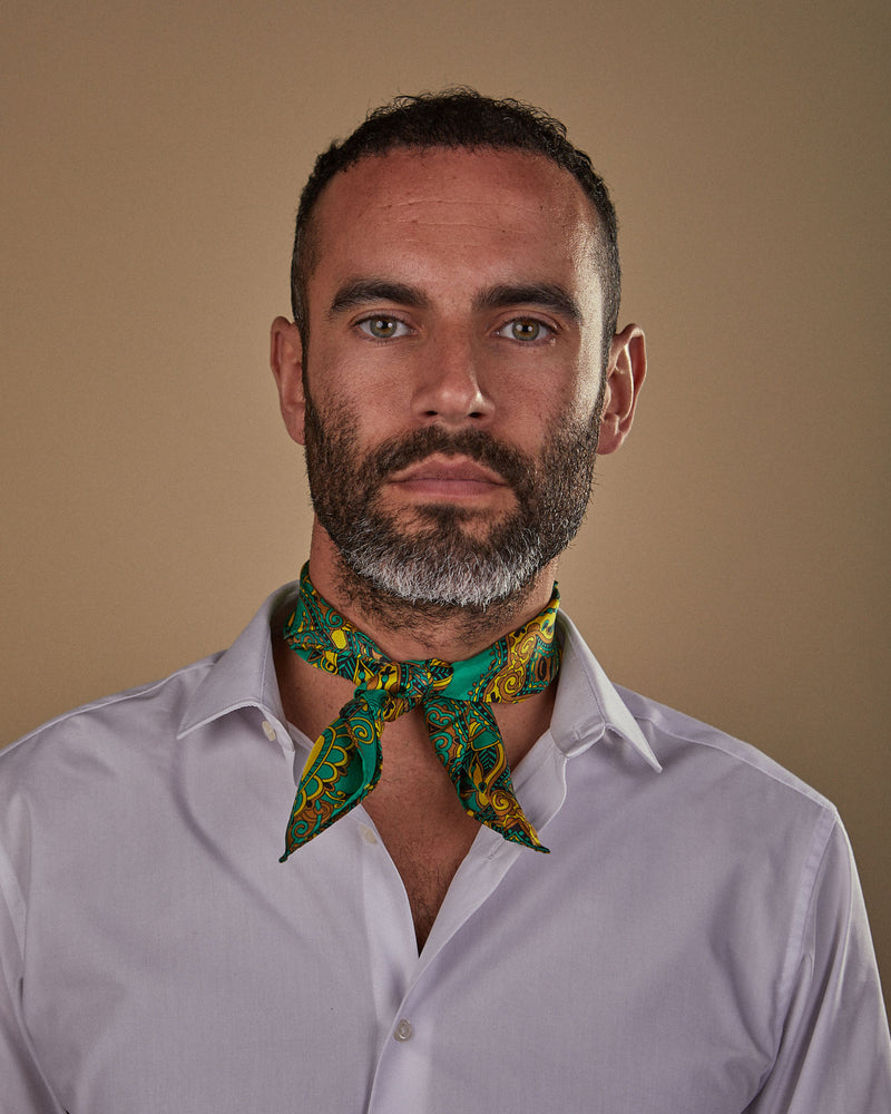 Portrait view of model looking straight ahead, wearing 'The Forks' golden Fleur de Lis patterned neckerchief on an emerald ground. Tied in a simple front-facing knot.