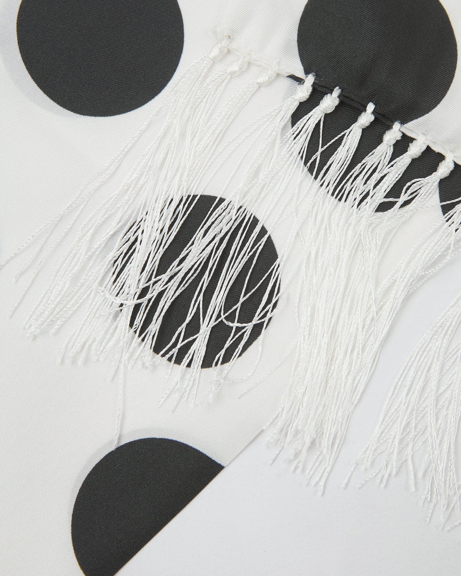 A close-up of the 'Gable' silk scarf, presenting a closer look at the black spots, white fringe and fine silk material.