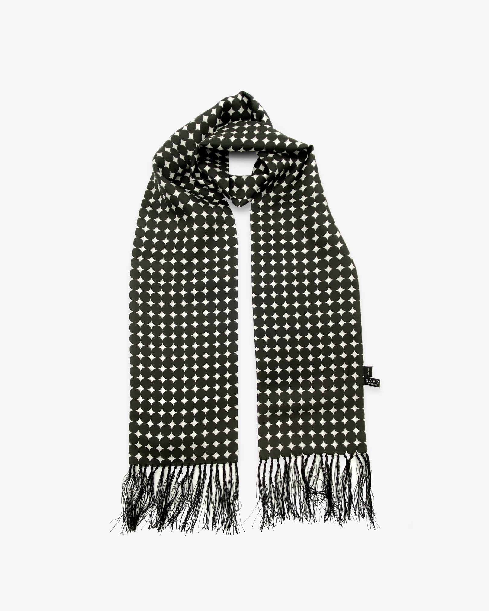 The Grant silk aviator scarf looped with both ends parallel to effectively display the black fringe and full repeat pattern of black discs on a white background.