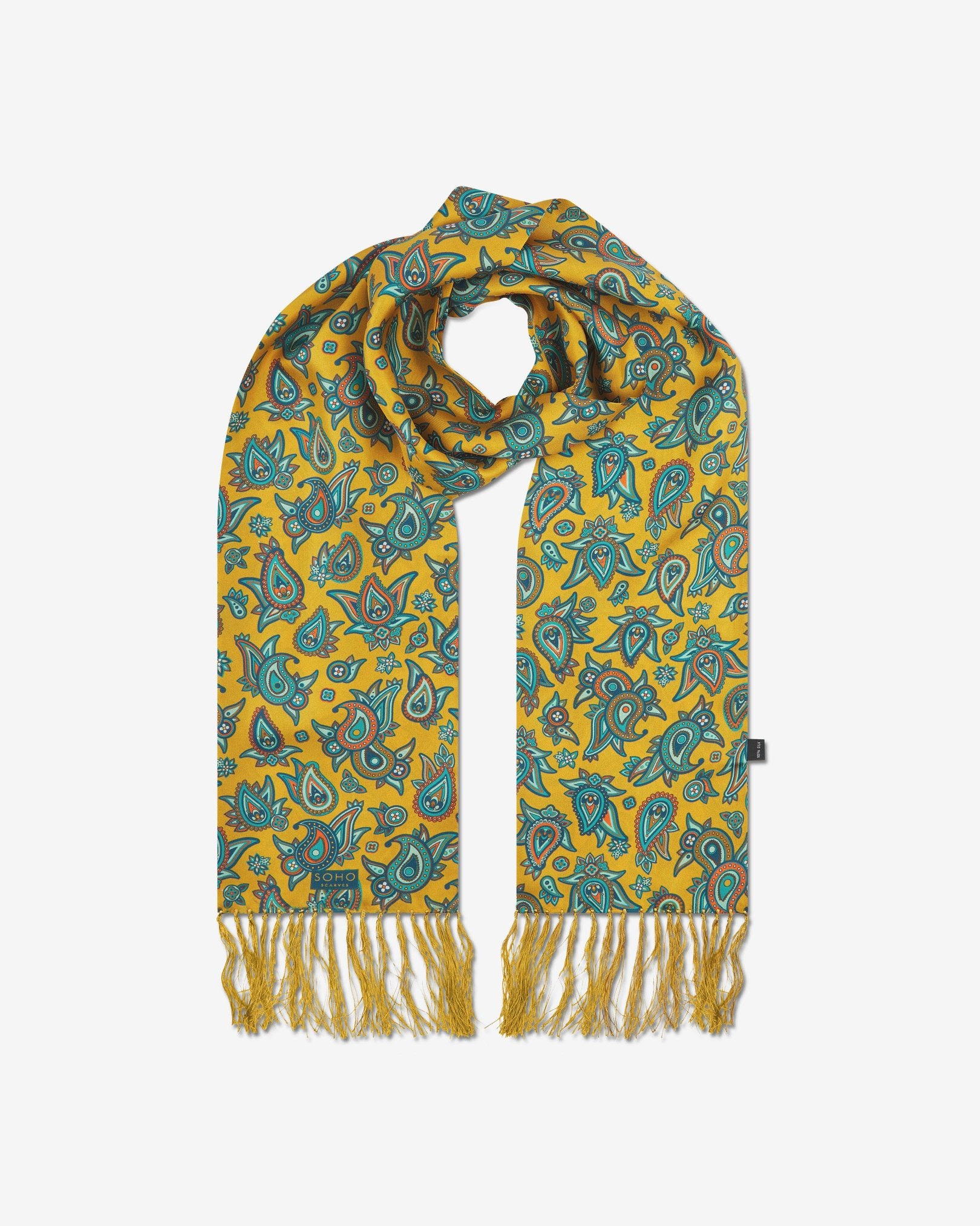 The 'Grassmere' gold silk aviator scarf looped with both ends parallel to effectively display the full repeat pattern of blue, blue-green, orange, and yellow paisley patterns on an gold background with matching fringes.