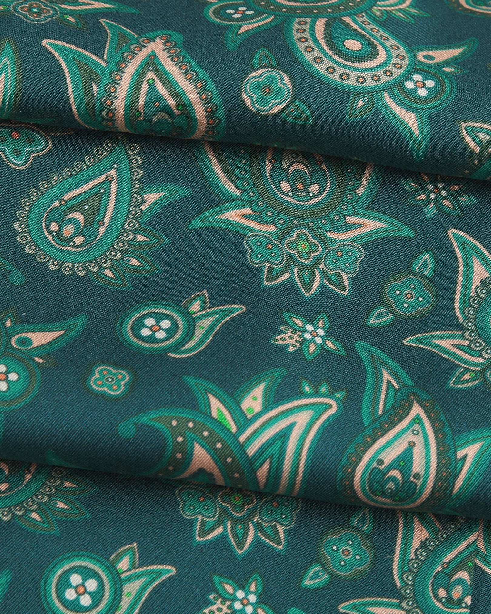 A ruffled close-up of the 'Grassmere' emerald-green silk aviator scarf, presenting the overlapping elements of green and salmon pink paisley patterns.