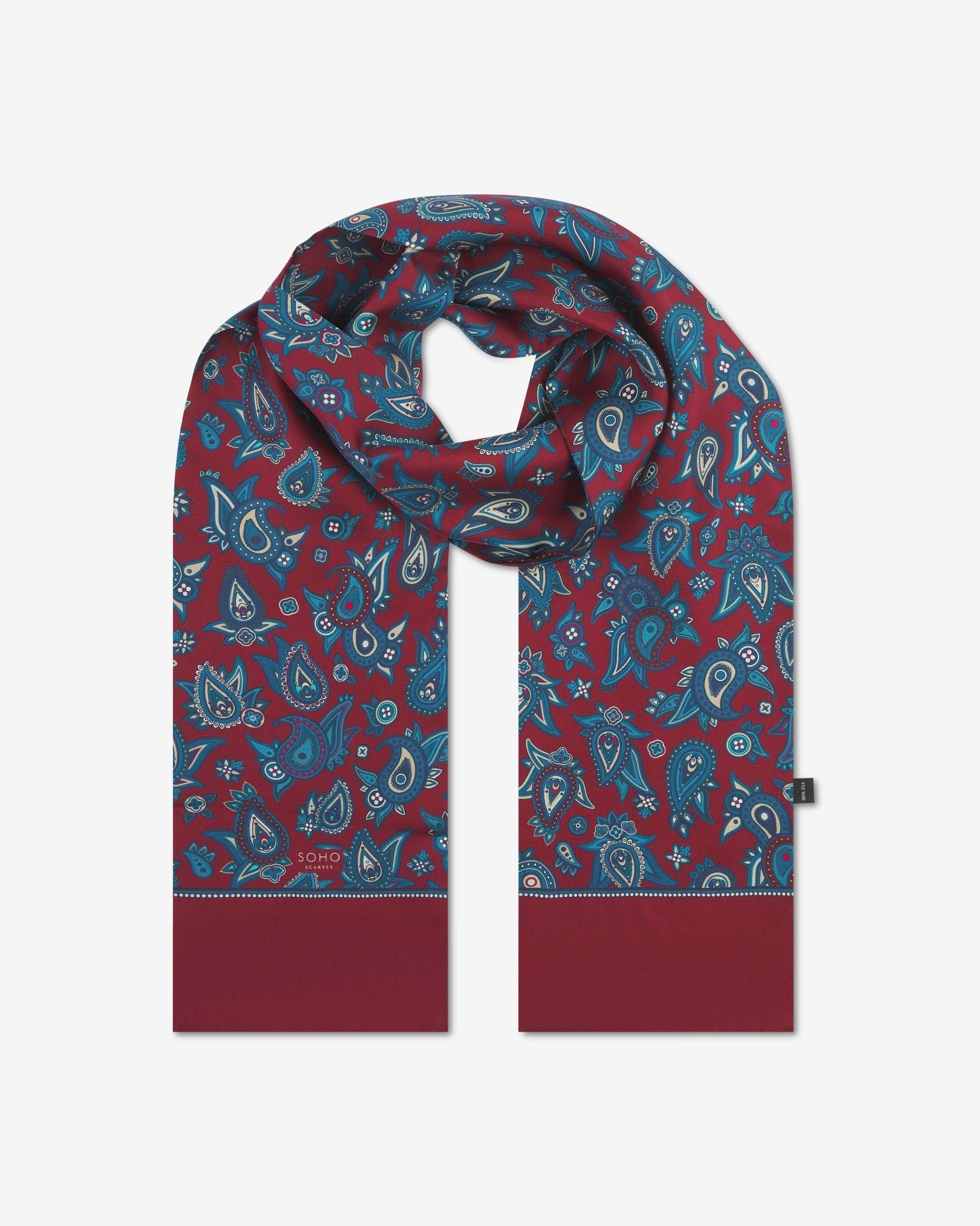 The 'Grassmere' rust silk scarf looped with both ends parallel to effectively display the full repeat pattern of blue and blue-green paisley patterns on an rust background.