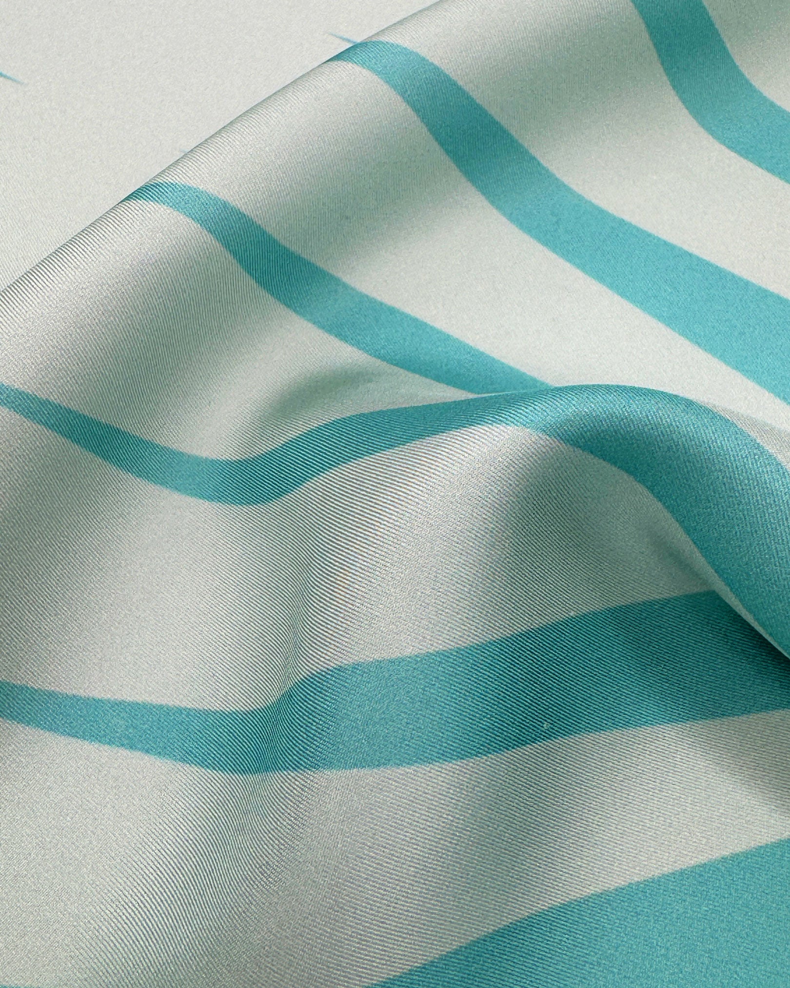 A ruffled close-up of the 'Hamburg' silk neckerchief, presenting a closer view of the waveform-like motif in teal and turquoise.