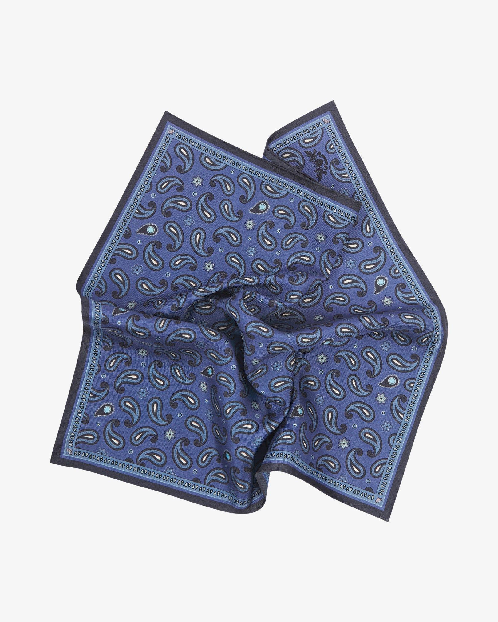 The 'Highbury' silk pocket square softly pinched and gathered at the centre, presenting the scattered paisley pattern in navy, slate and white on a rich cobalt-blue ground, framed by a fine repeating navy paisley border.