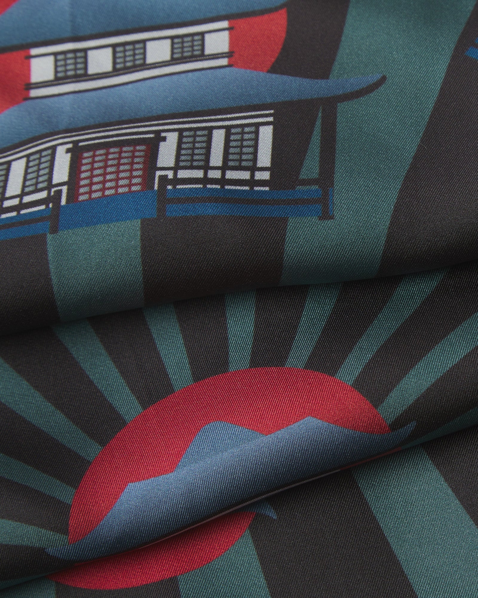 A ruffled close-up of the 'House' silk neckerchief, presenting a closer view of the house motif in green, blue and red on a black background and the fine silk weave.