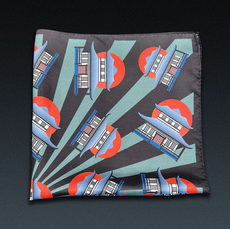 'The House' neckerchief folded into a quarter, showing multiple house motif in green, blue and red on a black background.