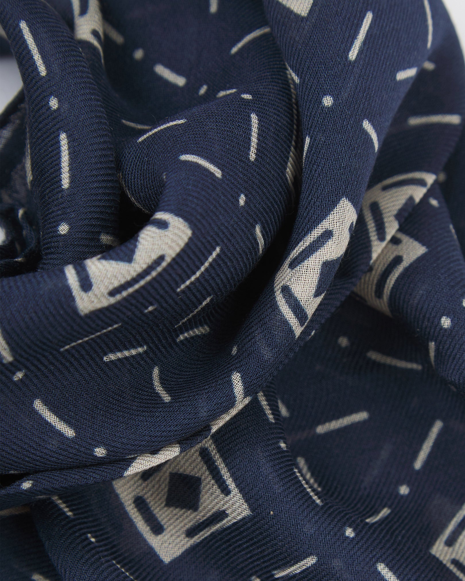 A ruffled close-up of the 'Diamonds' indigo bohemian wide scarf, showing the soft modal and wool blend fabric with an ordered diamond mosaic of white lozenges and crosshair motifs on an indigo blue background.