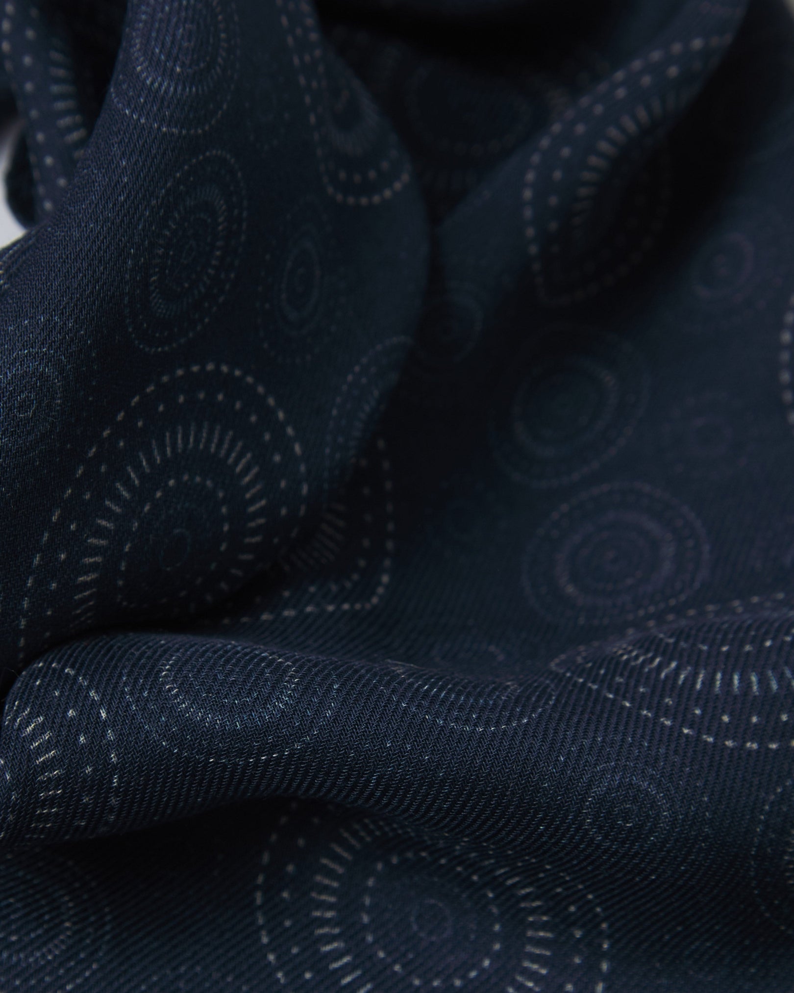 A ruffled close-up of the 'Circles' indigo bohemian wide scarf, showing the soft modal and wool blend fabric with concentric Op art-inspired disc motifs in white on a deep indigo-blue background.