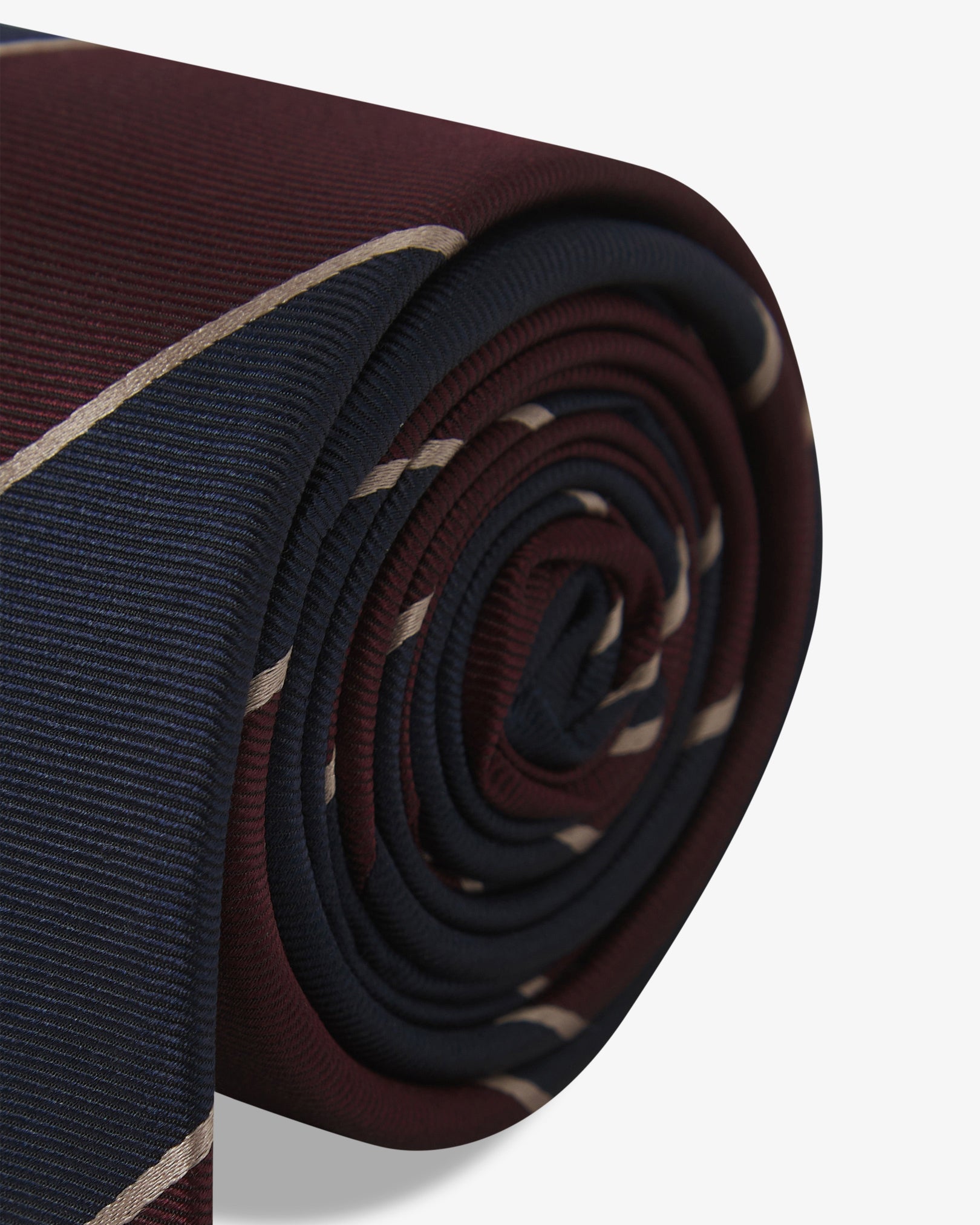The 'Jarrett Mahogany Haze' silk neck tie neatly coiled with a clear view of the silk weave and maroon and black bands with fine gold pinstripes.