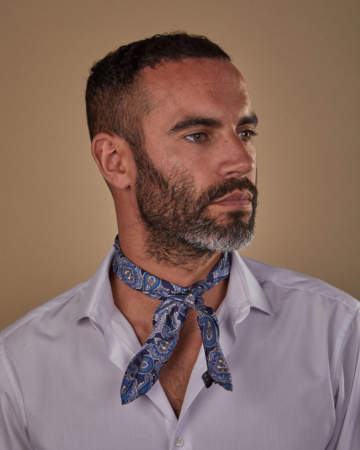 Portrait view of model looking to his left, wearing 'The DeZon' blue paisley neckerchief tied in a simple front-facing knot.