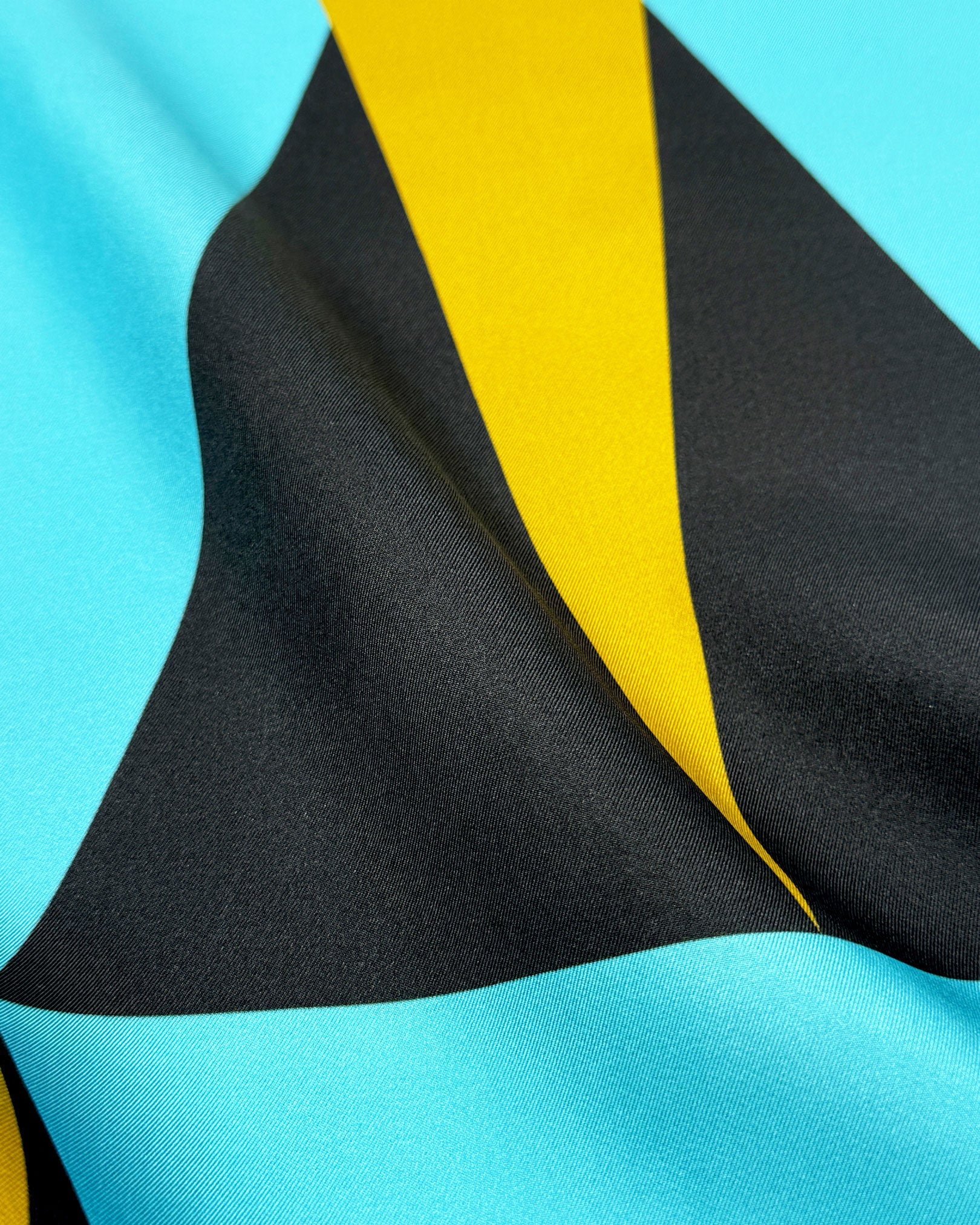 A ruffled close-up of the 'Leipzig' silk neckerchief, presenting a closer view of the interplay of blue, grey and yellow triangles.