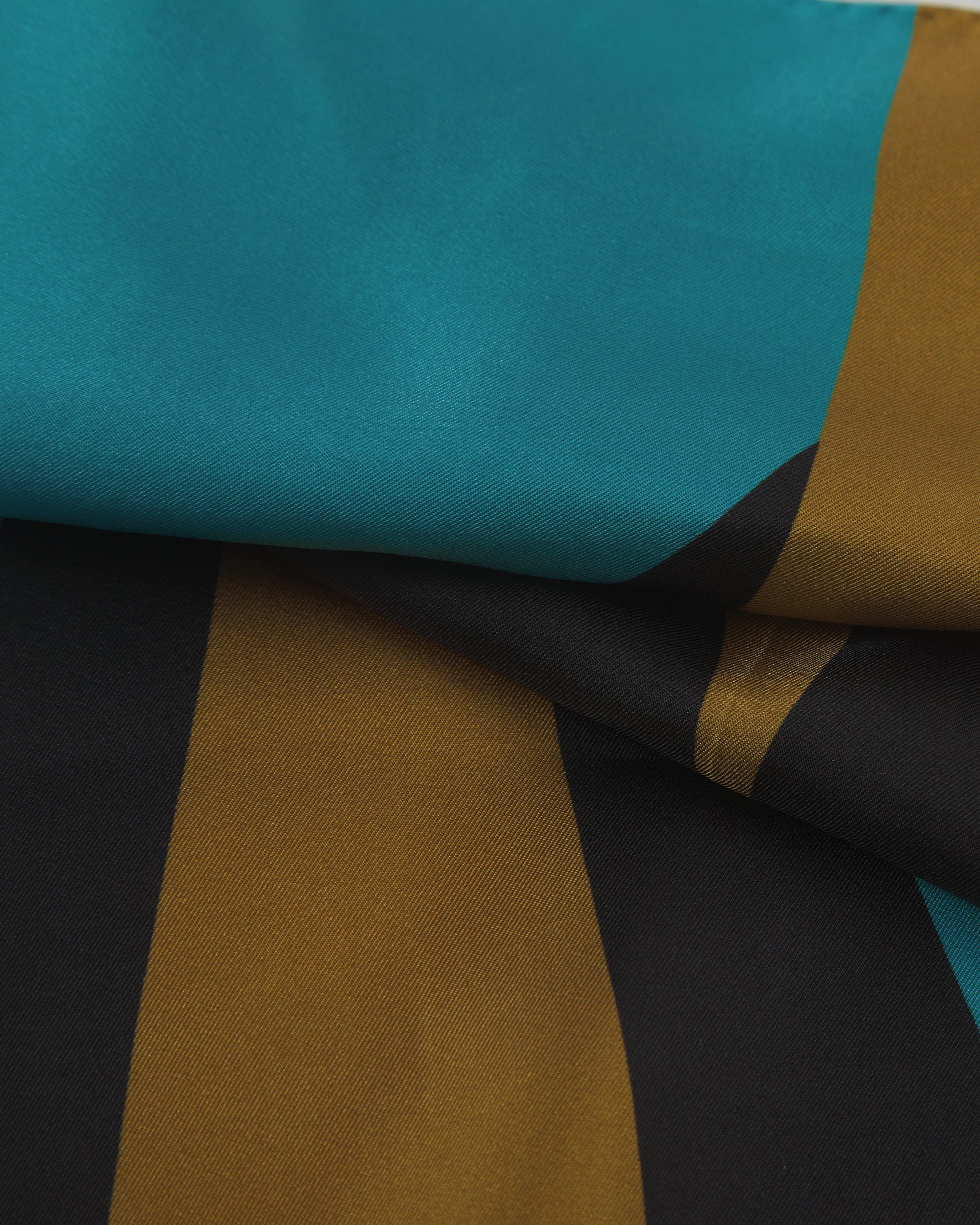 A ruffled close-up of the 'Leipzig' silk neckerchief, presenting a closer view of the interplay of blue, grey and yellow triangles.