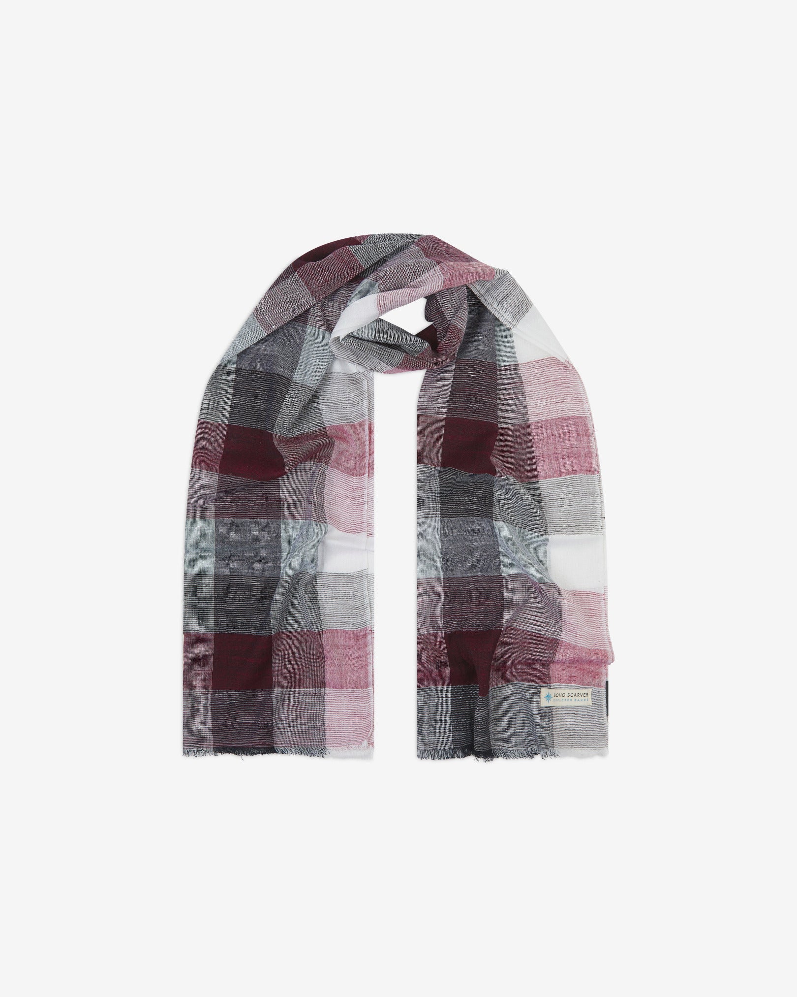 The 'Fiennes' cotton plaid scarf, looped in middle with both ends parallel. Displaying the checkered pattern of greys, pinks, and whites and the SOHO Scarves Explorer Range branding logo in the bottom-right.