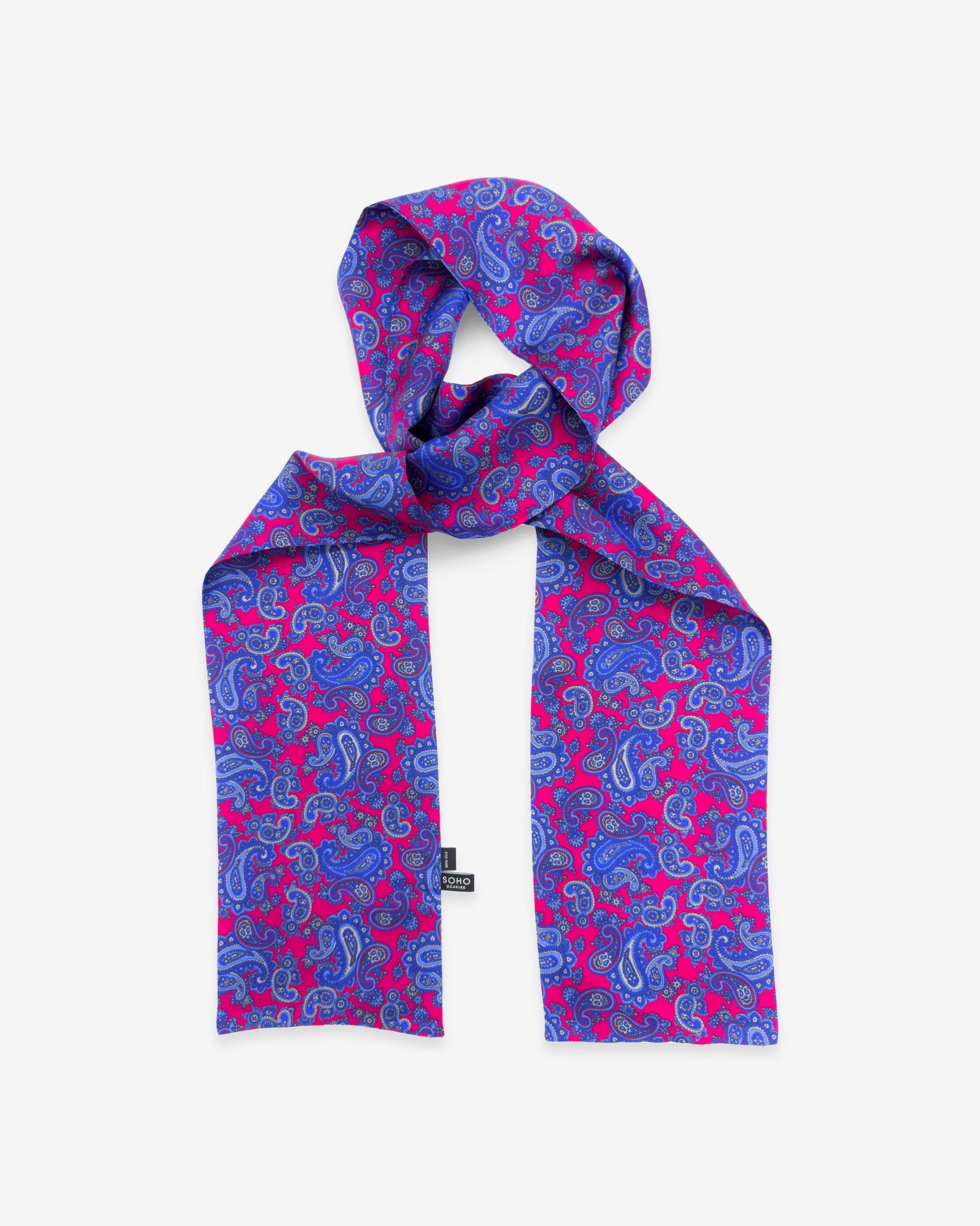 'The Kita' paisley patterned silk scarf arranged in a rectangular shape, clearly showing the fuchsia fabric with blue-violet paisley patterns and the 'Soho Scarves' branding label on the bottom left edge.