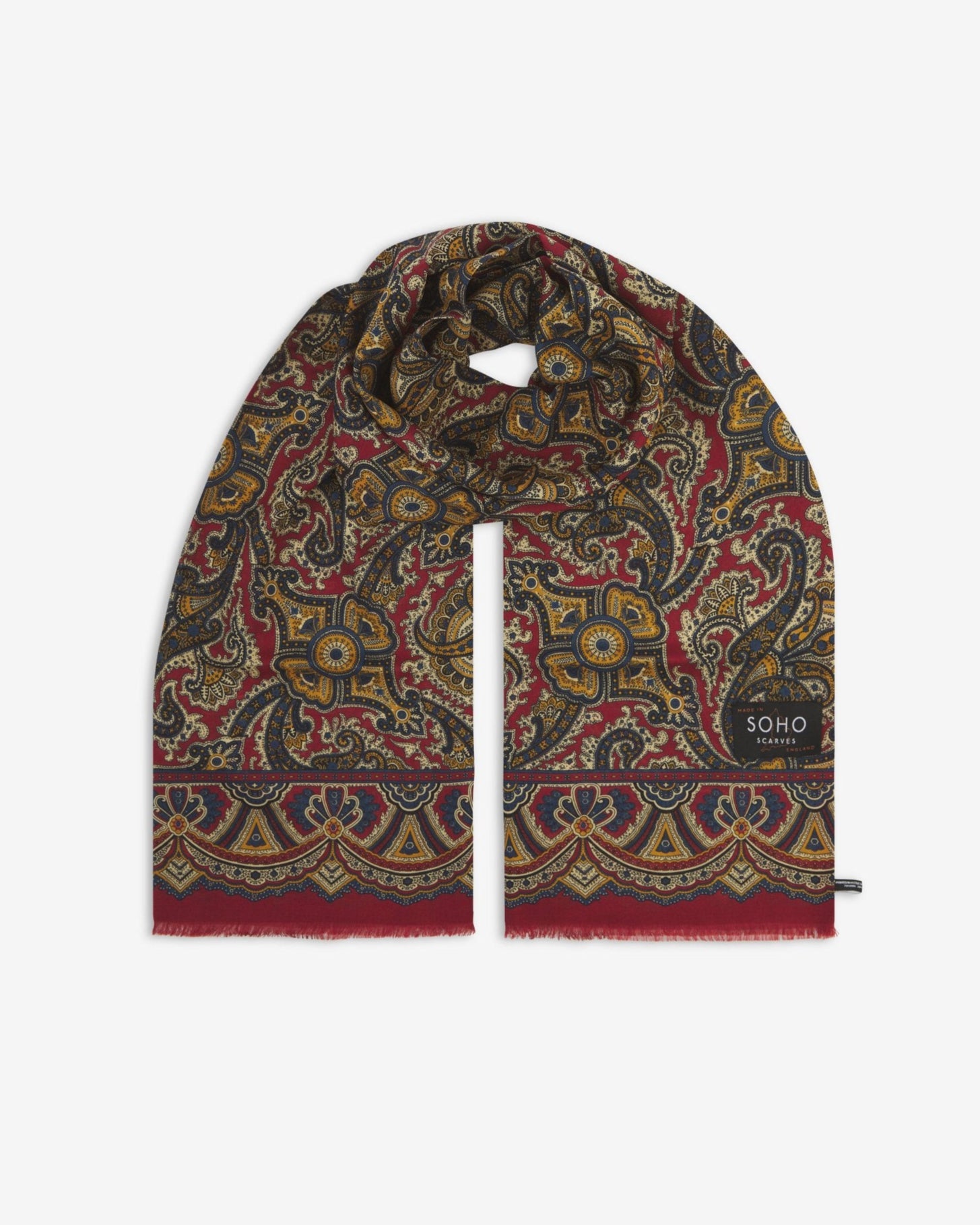 Premium deep red paisley silk-wool scarf unravelled and looped in the middle, presenting slightly longer and wider scarf dimensions, ornate border, eyelash fringing and ‘Soho Scarves’ label.