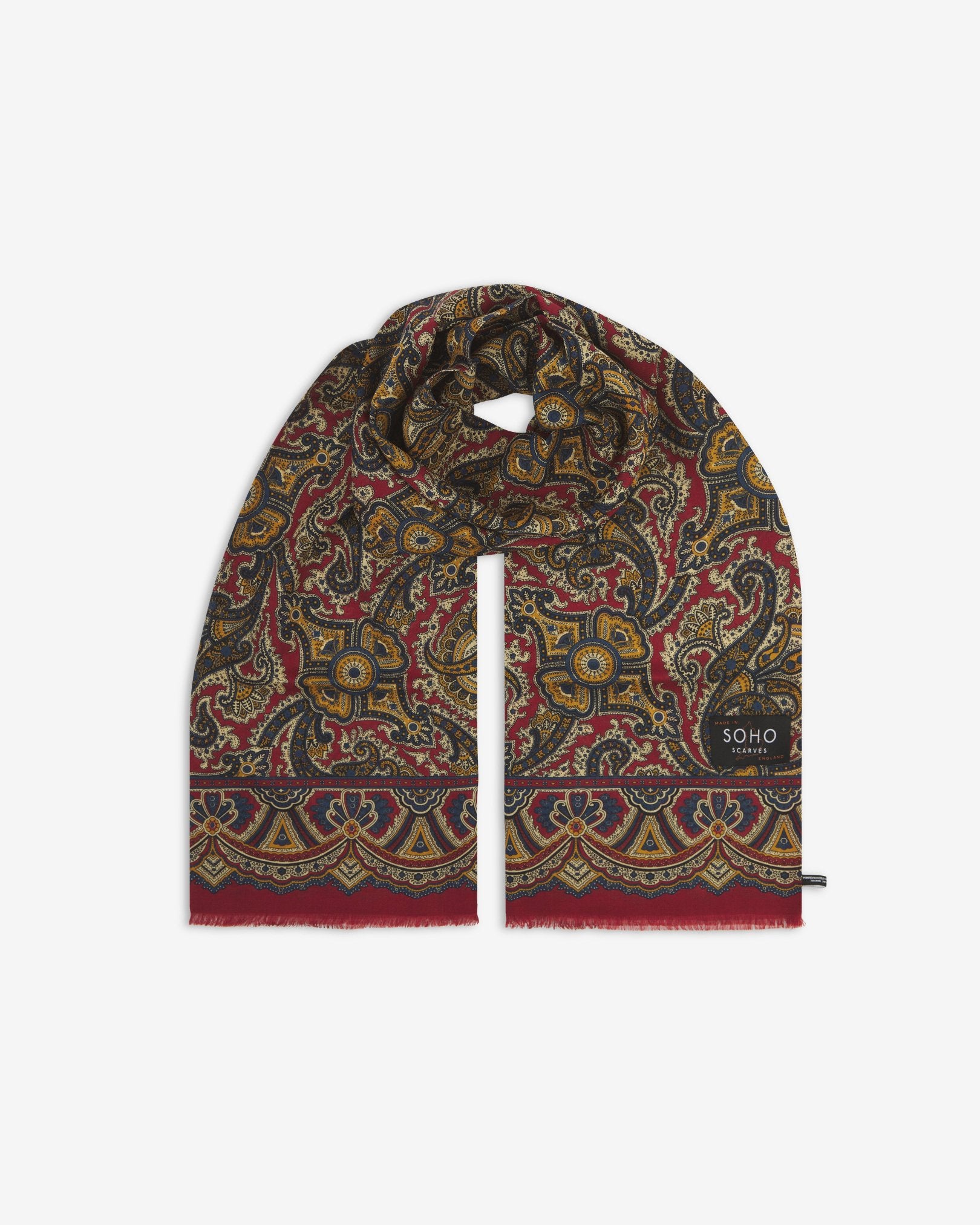 Premium deep red paisley silk-wool scarf unravelled and looped in the middle, presenting slightly longer and wider scarf dimensions, ornate border, eyelash fringing and ‘Soho Scarves’ label.