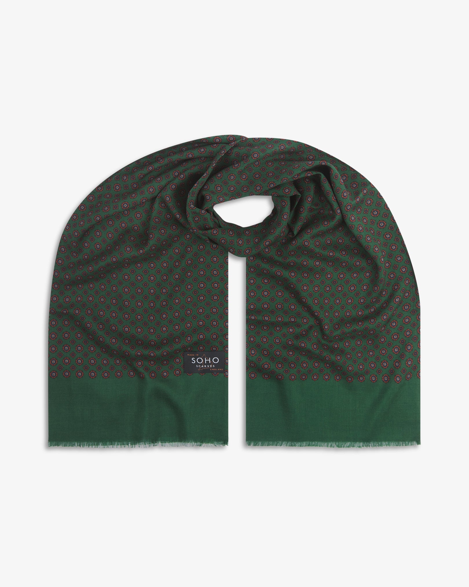 Premium green and orange silk-wool scarf with geometric floral repeat. Unravelled and looped in the middle, presenting slightly longer and wider scarf dimensions, ornate border and 'Soho Scarves' label.