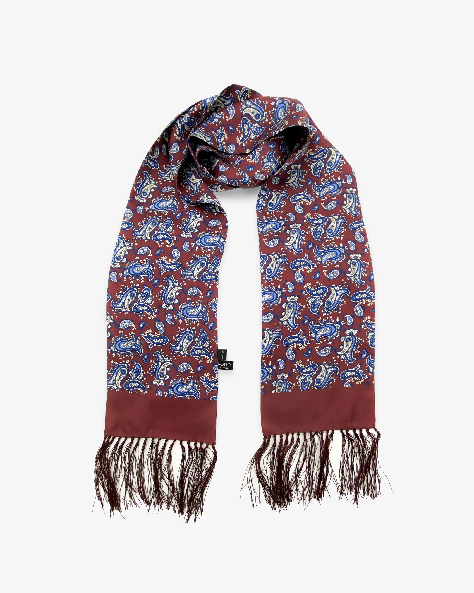 The Vancouver Aviator burgundy silk scarf with royal blue and cream paisley patterns, scarf looped in middle with both ends parallel clearly showing the deep-burgundy 3-inch fringe and the 'Soho Scarves' label.